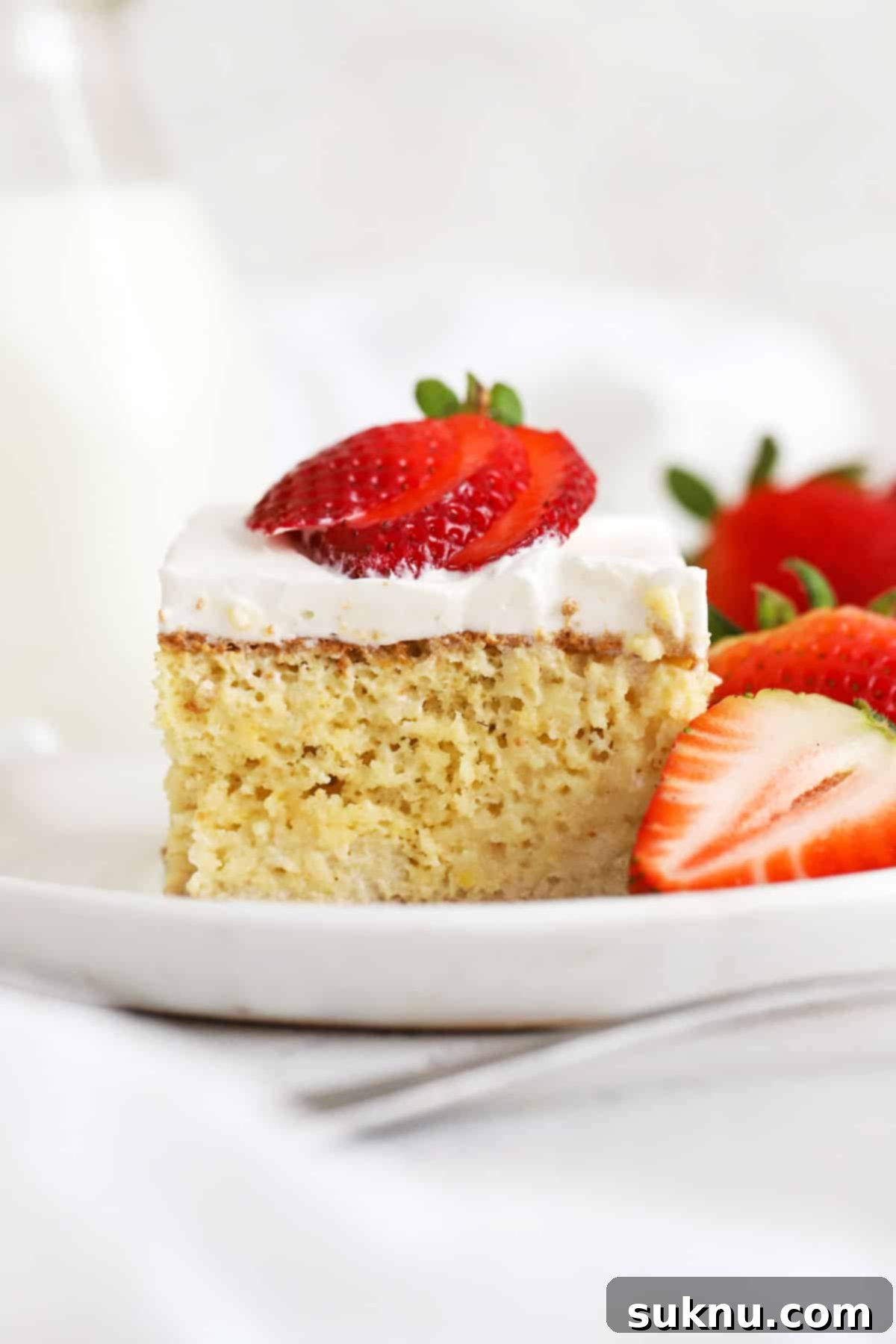 A beautifully sliced gluten-free tres leches cake, topped with fresh strawberries, resting on a white plate.