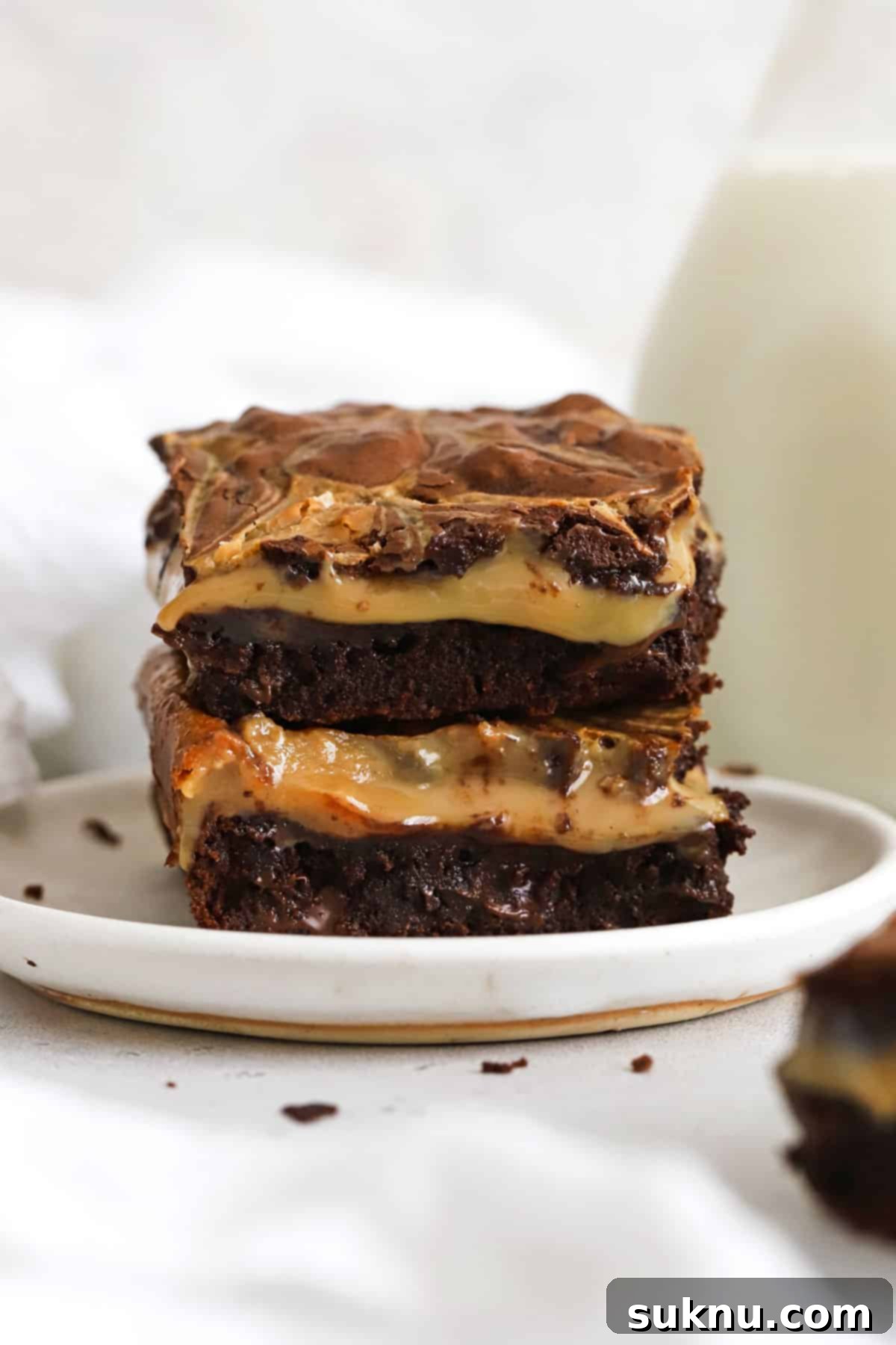 Stacked fudgy gluten-free dulce de leche brownies on a white plate, showcasing their rich texture and caramel swirls.