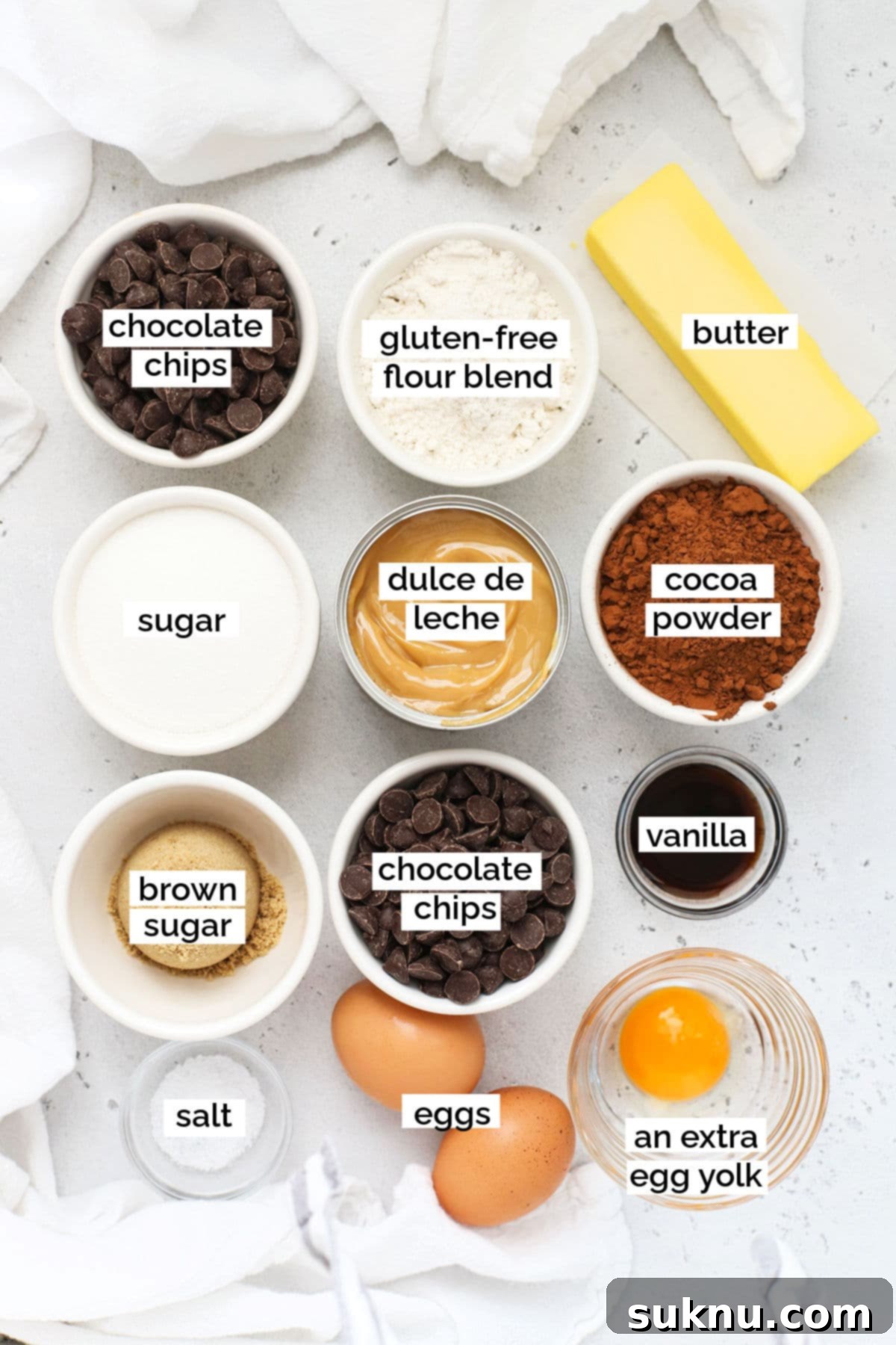 Ingredients laid out for making gluten-free dulce de leche brownies: butter, chocolate chips, sugars, eggs, vanilla, gluten-free flour, cocoa powder, salt, and dulce de leche.