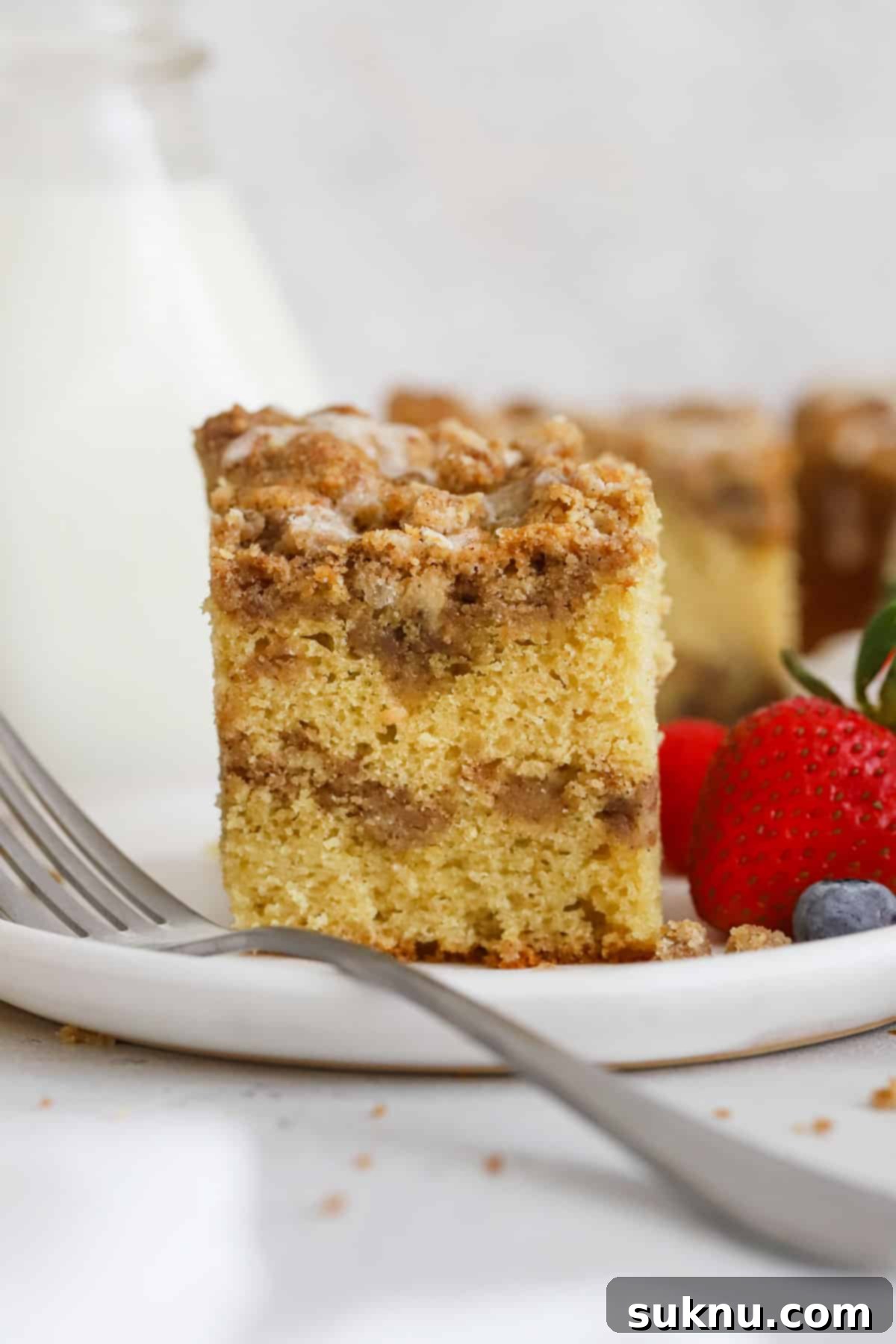 A slice of delicious gluten-free cinnamon crumb cake on a white plate, garnished with fresh berries.