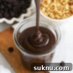 Close-up of thick homemade hot fudge sauce being poured into a glass jar, showcasing its rich texture.