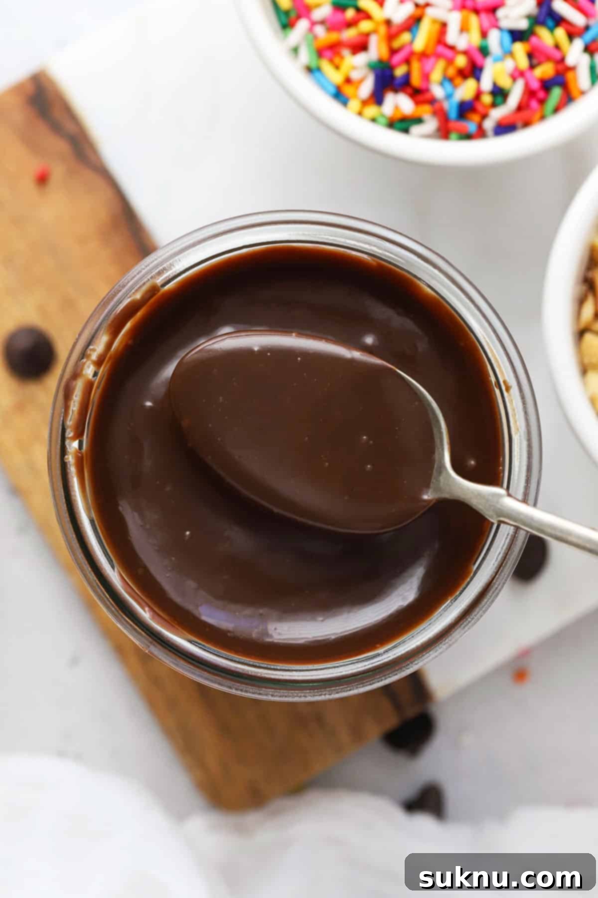 A spoon scooping thick, dark homemade hot fudge sauce out of a glass jar, highlighting its rich texture.
