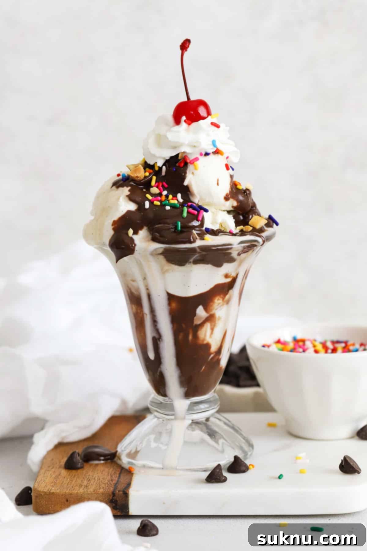 A classic hot fudge sundae piled high with vanilla ice cream, hot fudge, whipped cream, sprinkles, nuts, and a maraschino cherry.