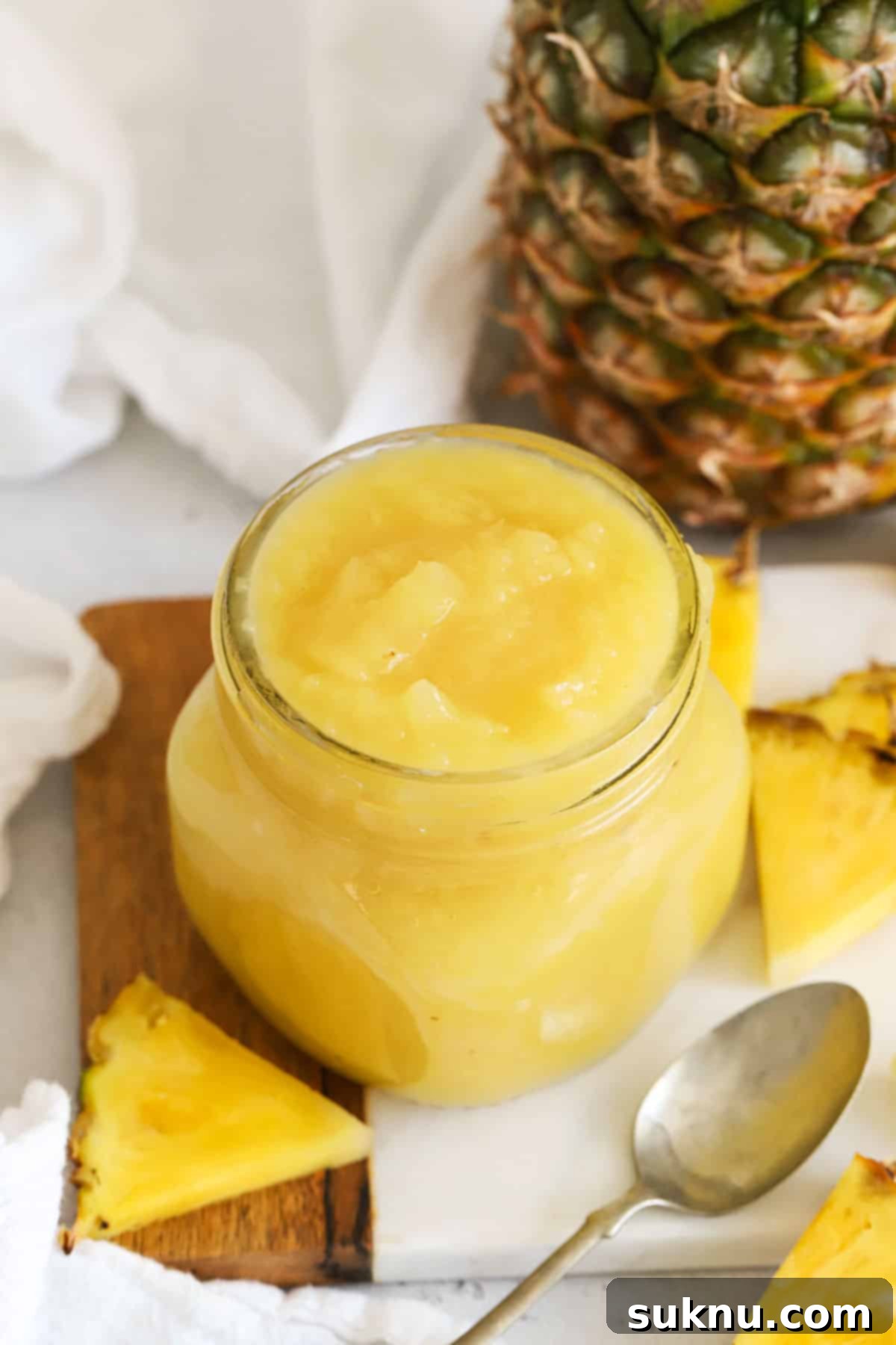 Homemade pineapple ice cream topping in a glass jar next to fresh pineapple slices