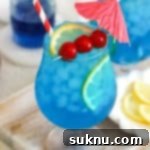 Azure Lagoon Cooler 11 Two vibrant blue lagoon mocktails in elegant hurricane glasses, ready to be enjoyed.