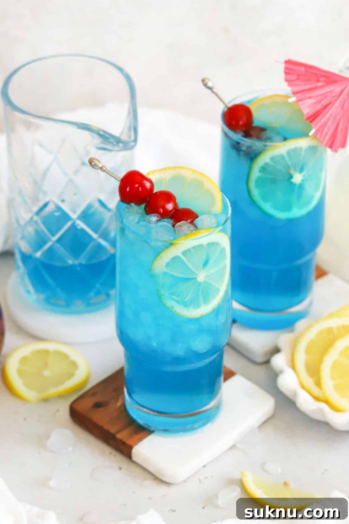 Azure Lagoon Cooler 6 Two tall glasses of non-alcoholic Blue Lagoon mocktails, garnished with fruit, sitting on a wooden table, emphasizing their refreshing appeal.