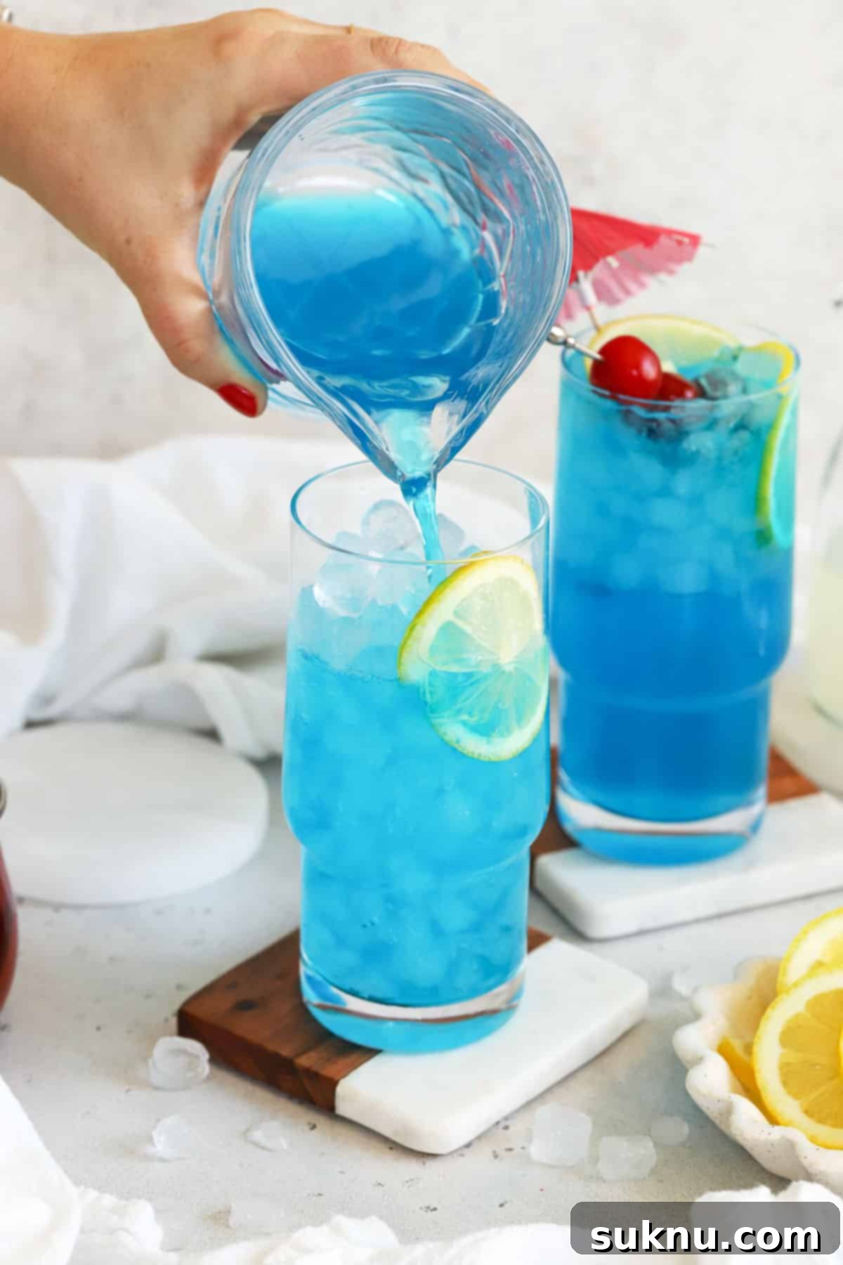 Azure Lagoon Cooler 7 A clear glass being filled with a Virgin Blue Lagoon mocktail, showcasing the vibrant blue color as the drink is poured over ice.