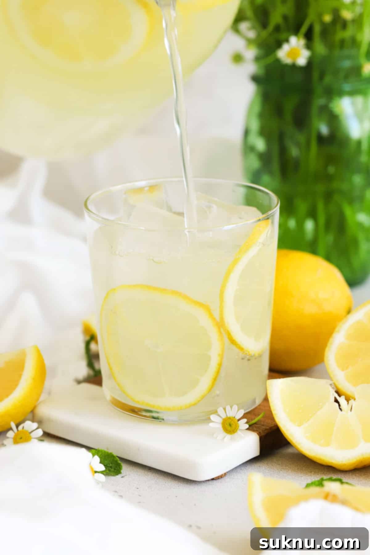 Refreshing Homemade Lemonade 6 A hand gently pouring homemade lemonade from a pitcher into a glass filled with ice and garnishes.