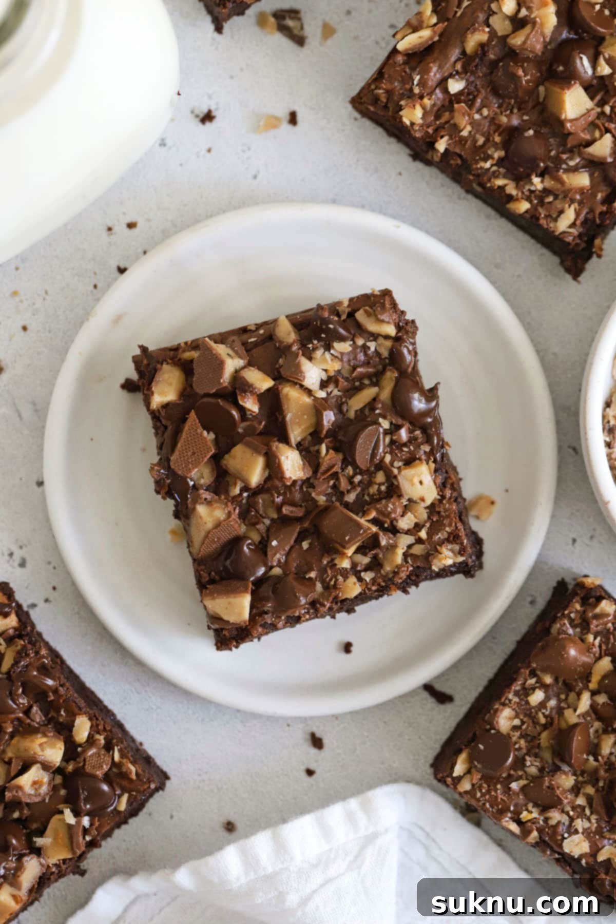 Decadent Gluten-Free Toffee Brownies 8 An appetizing close-up of gluten-free toffee brownies alongside a glass of milk and a bowl of extra toffee pieces, emphasizing their delightful crispness.