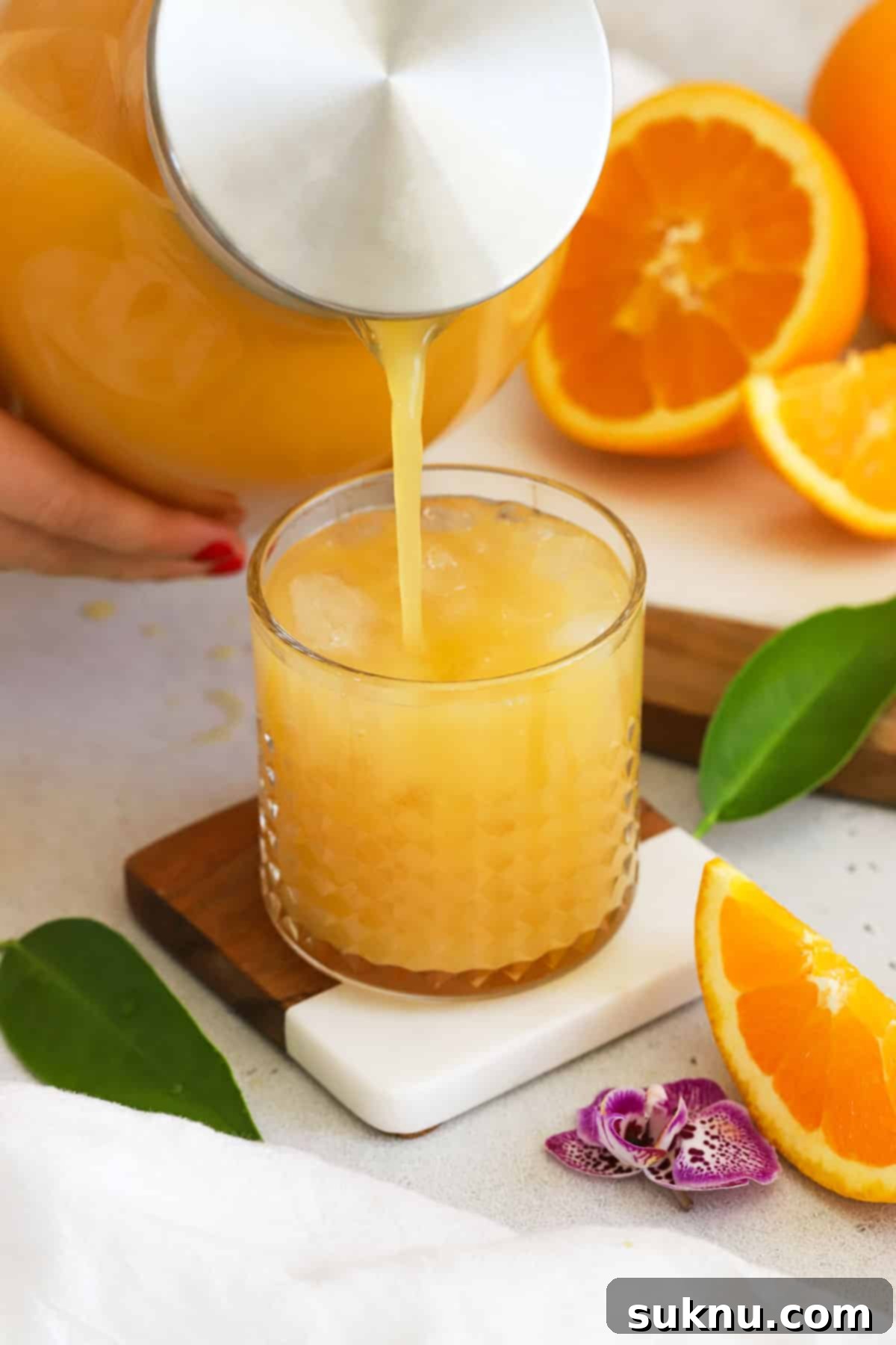 A hand pouring vibrant homemade POG juice into a glass over ice