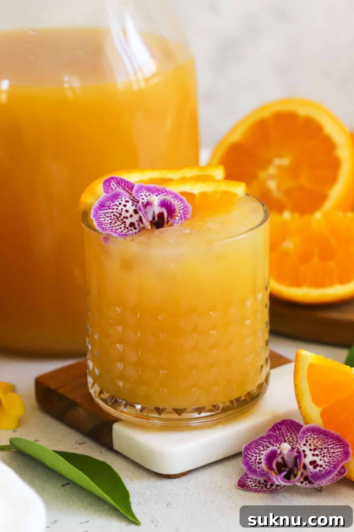 A glass of POG juice garnished beautifully with a purple edible flower and fresh orange slices