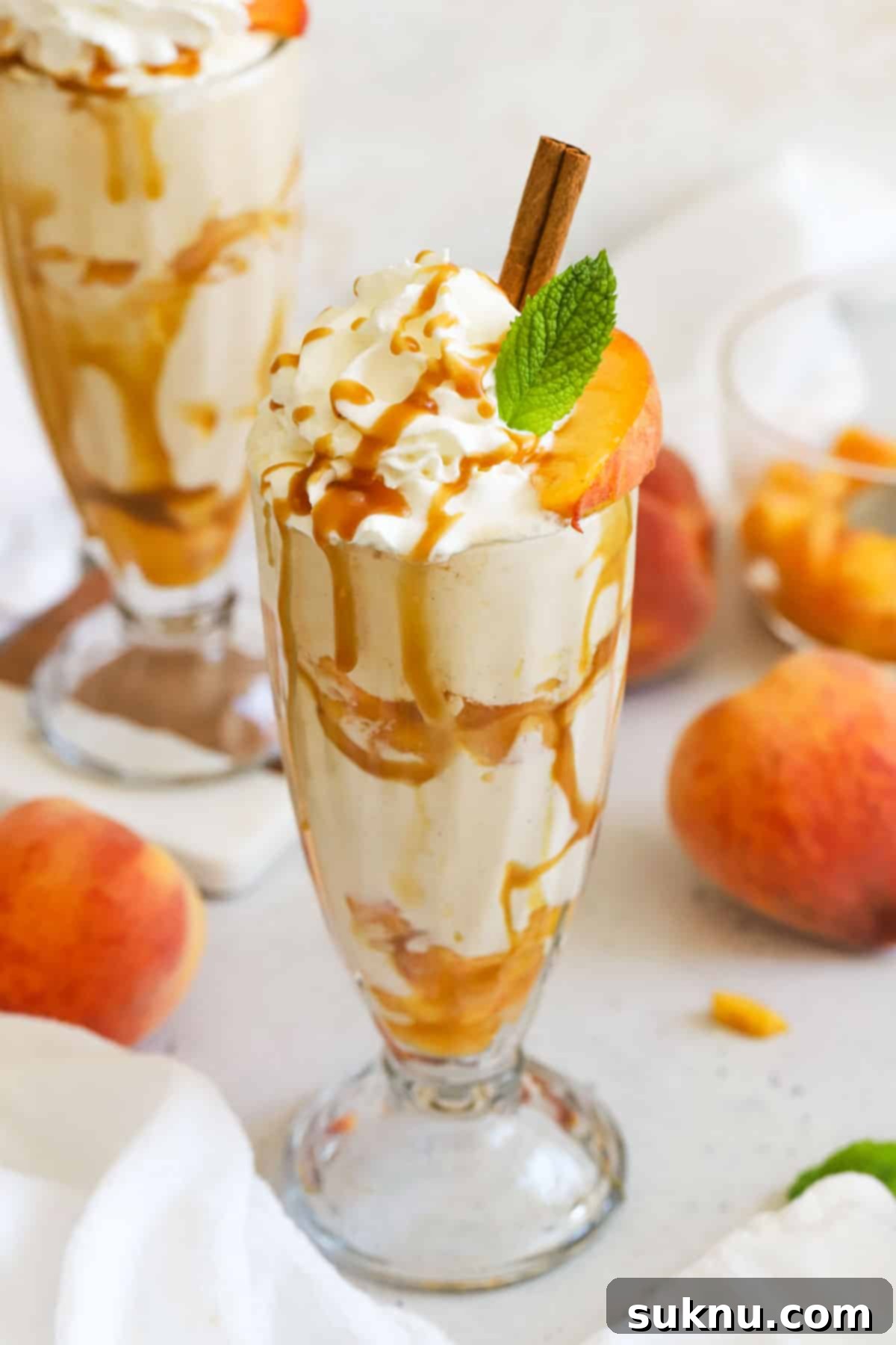 Peachy Dream Shake 2 Two homemade peach milkshakes in tall milkshake glasses, garnished with whipped cream and peach slices.