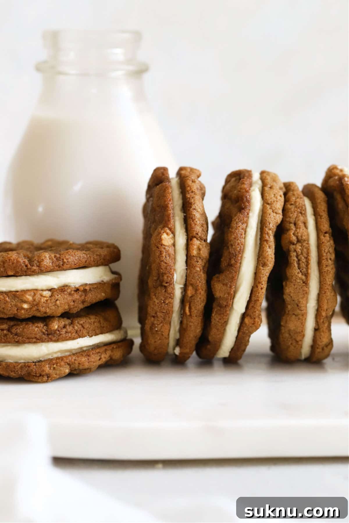 Gluten-free oatmeal cream pies stacked next to a bottle of milk, ready to be enjoyed