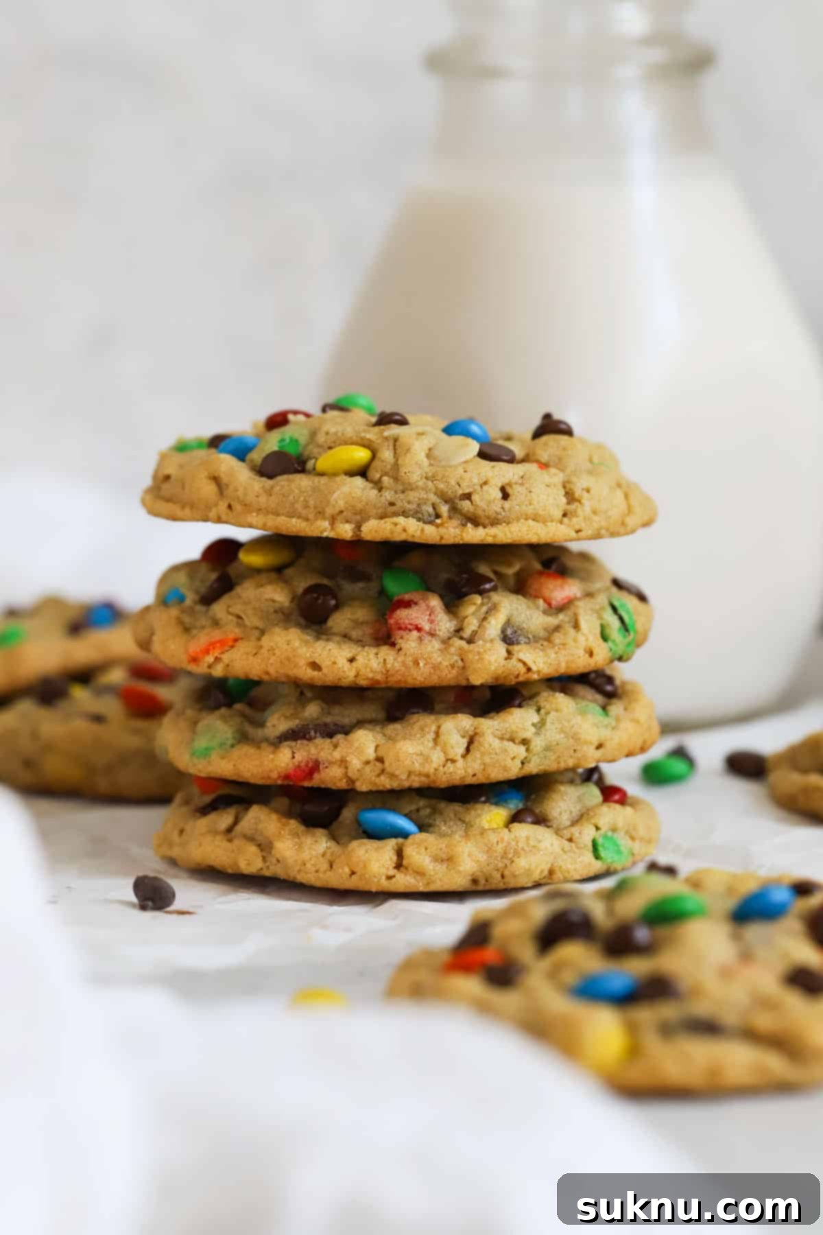 A stack of golden-brown gluten-free monster cookies next to a bottle of milk, highlighting their delicious appeal.