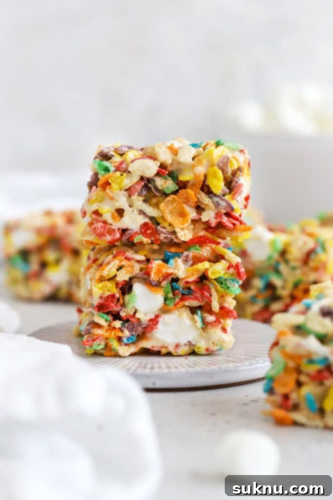 two fruity pebble rice krispies treats stacked on a white dessert plate