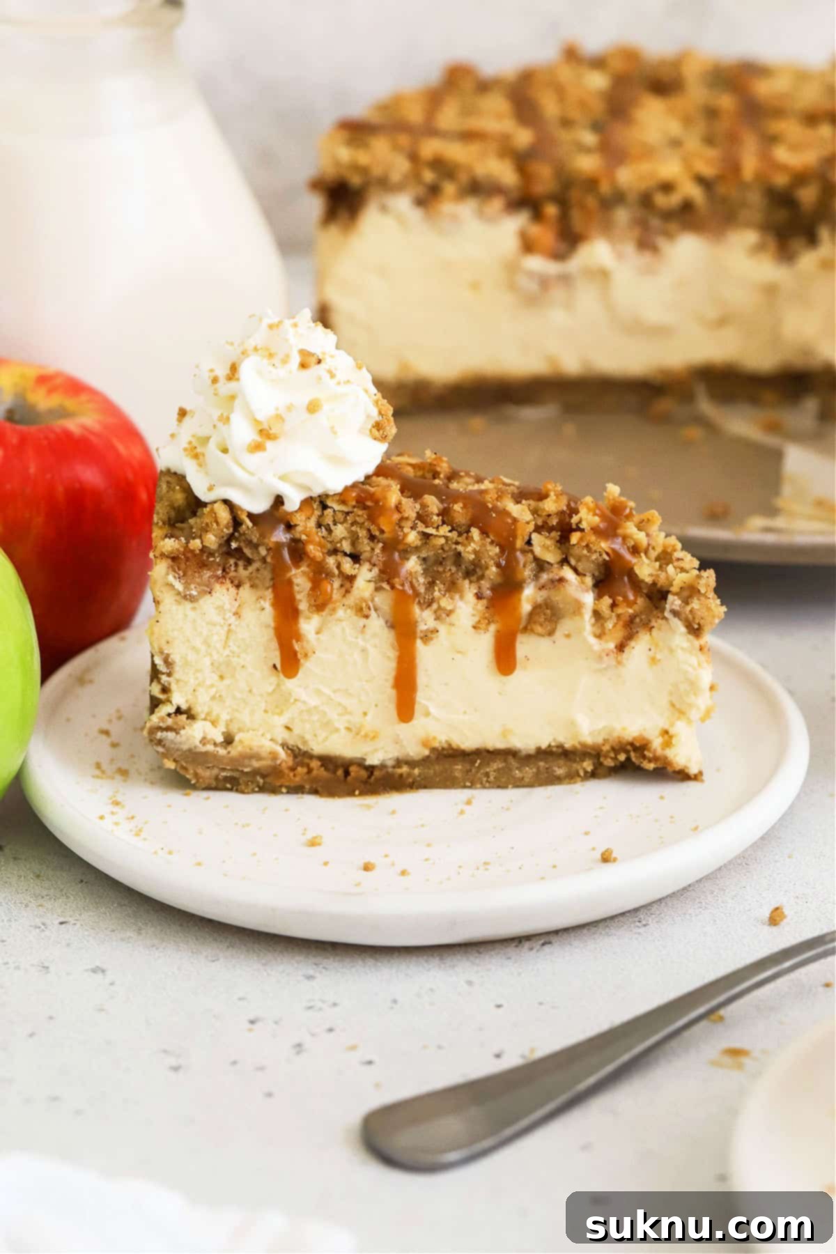 Slice of gluten-free caramel apple crumble cheesecake topped with whipped cream, ready to be enjoyed.