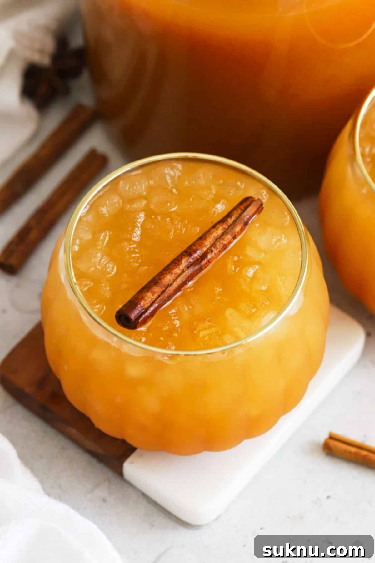 Enchanted Pumpkin Elixir 2 Two pumpkin-shaped glasses filled with golden pumpkin juice, garnished with cinnamon sticks, evoking a magical autumn atmosphere.