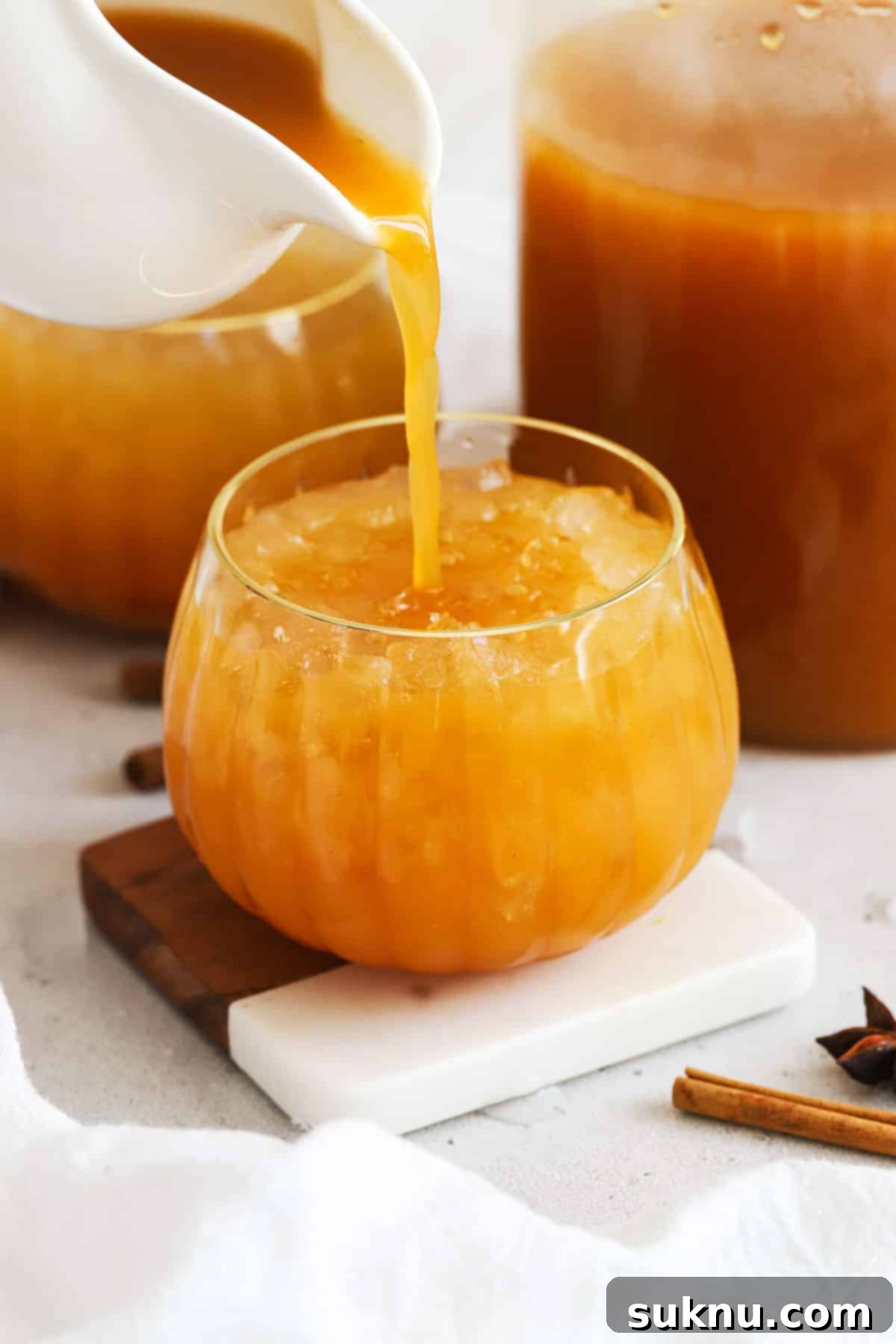 Enchanted Pumpkin Elixir 5 Someone pouring golden pumpkin cider into a clear, pumpkin-shaped glass, highlighting its inviting color.