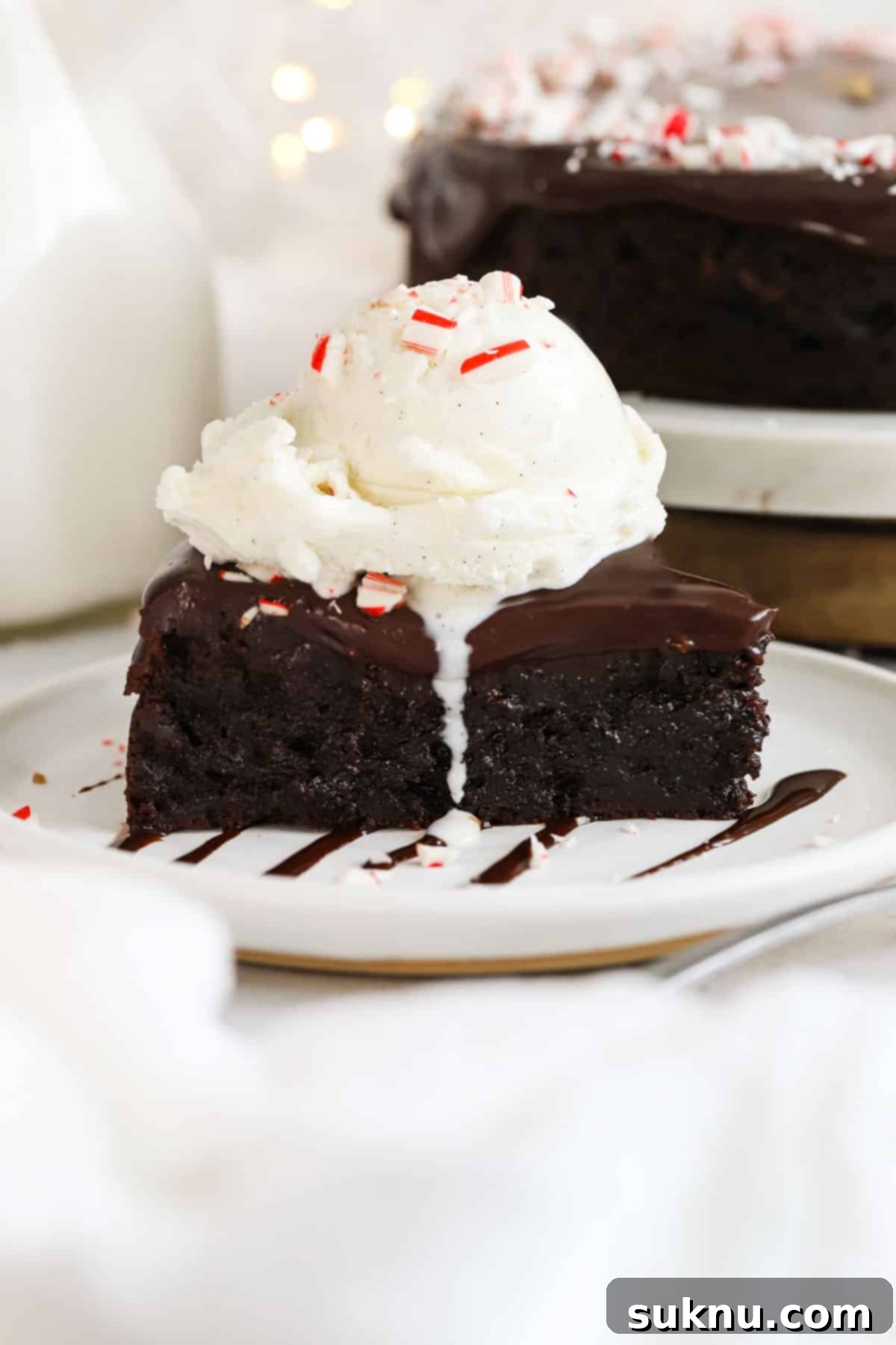 A decadent slice of peppermint flourless chocolate cake topped with a scoop of vanilla ice cream and a sprinkle of crushed peppermint candy, beautifully presented for a holiday celebration.