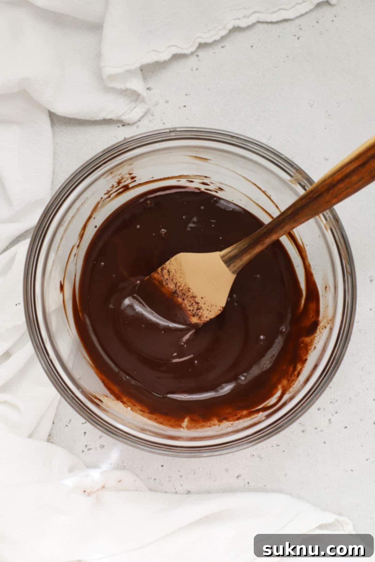 A beautiful glass bowl filled with rich, glossy peppermint chocolate ganache, perfectly prepared and ready to be poured over the cooled cake.