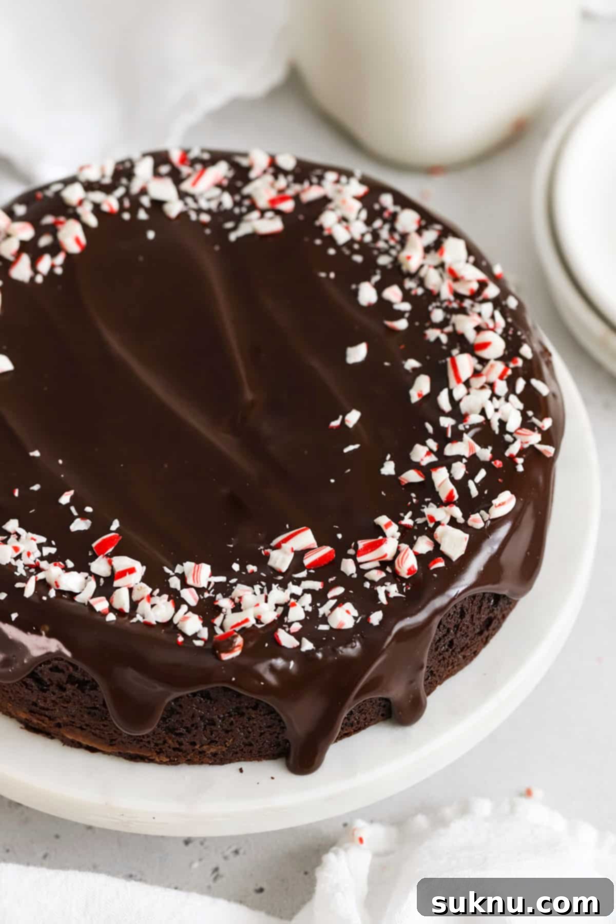 A beautifully presented peppermint flourless chocolate cake on a white marble cake stand, elegantly garnished with a generous sprinkle of crushed peppermint candy, ready for a festive gathering.