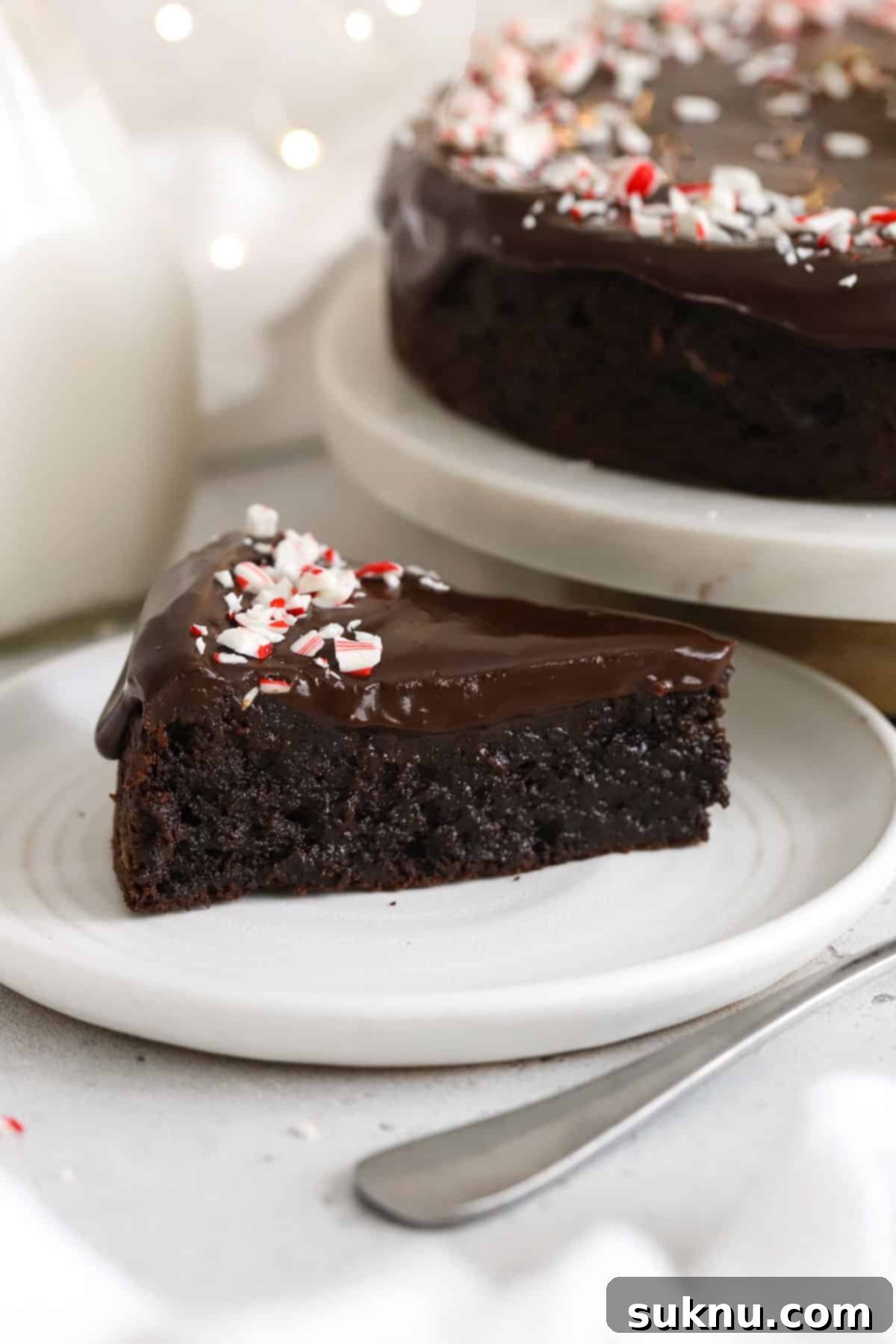 A perfectly sliced piece of peppermint flourless chocolate cake on a pristine white dessert plate, showcasing its dense, fudgy texture and glistening ganache topping, ready to be enjoyed.