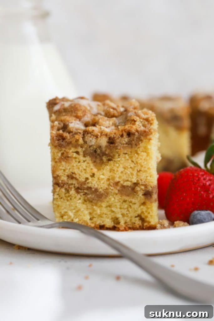 A slice of gluten-free cinnamon crumb coffee cake on a white plate, garnished with fresh berries.