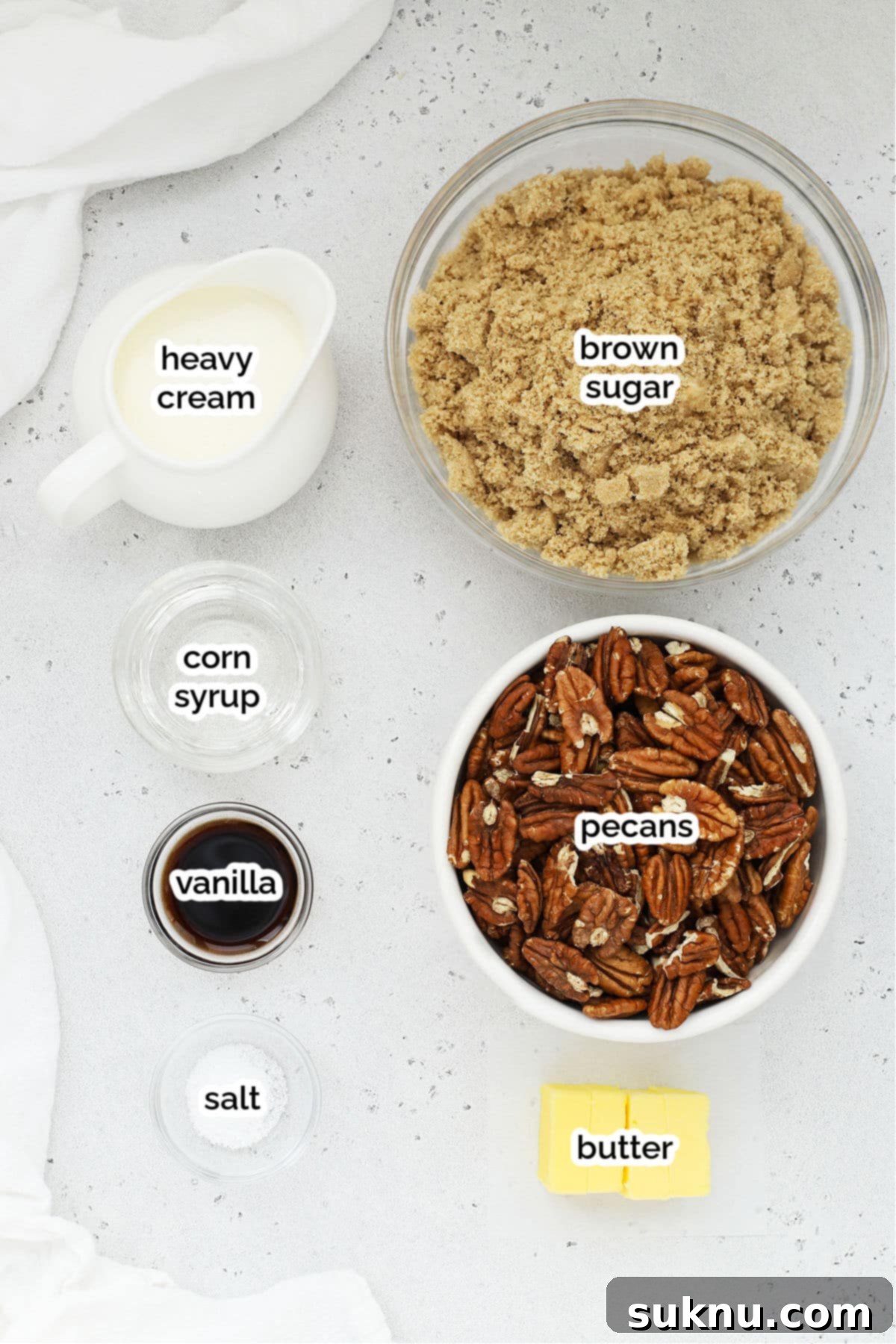 A collection of ingredients for homemade pecan pralines, including pecans, brown sugar, heavy cream, corn syrup, salt, butter, and vanilla extract.