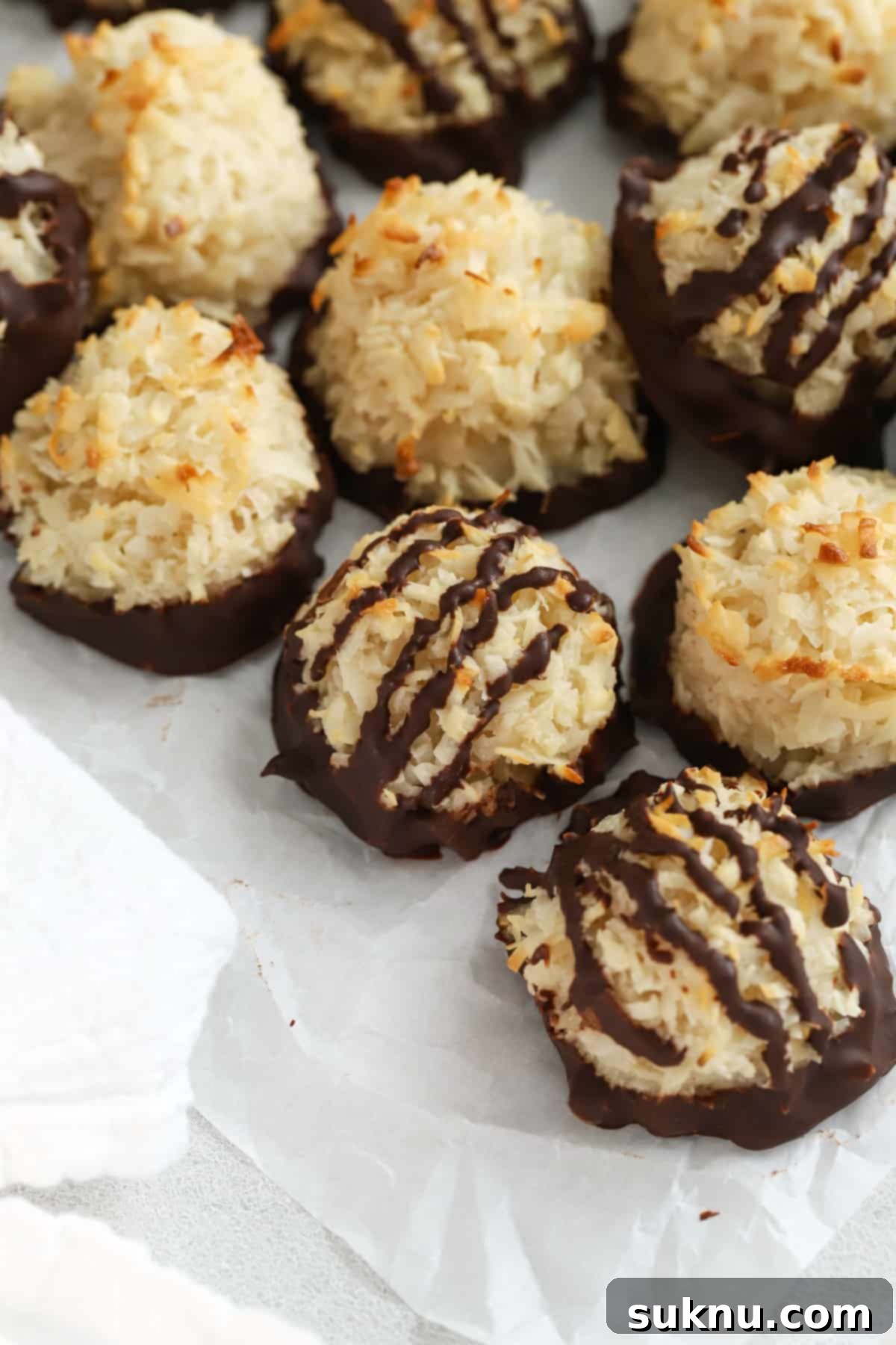 Gluten-free coconut macaroons cooling on parchment paper, half dipped in chocolate.