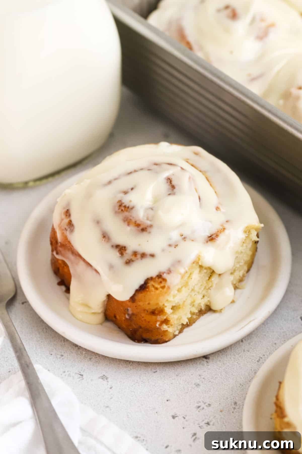 Gluten-free cinnamon roll on a white plate next to a bottle of milk