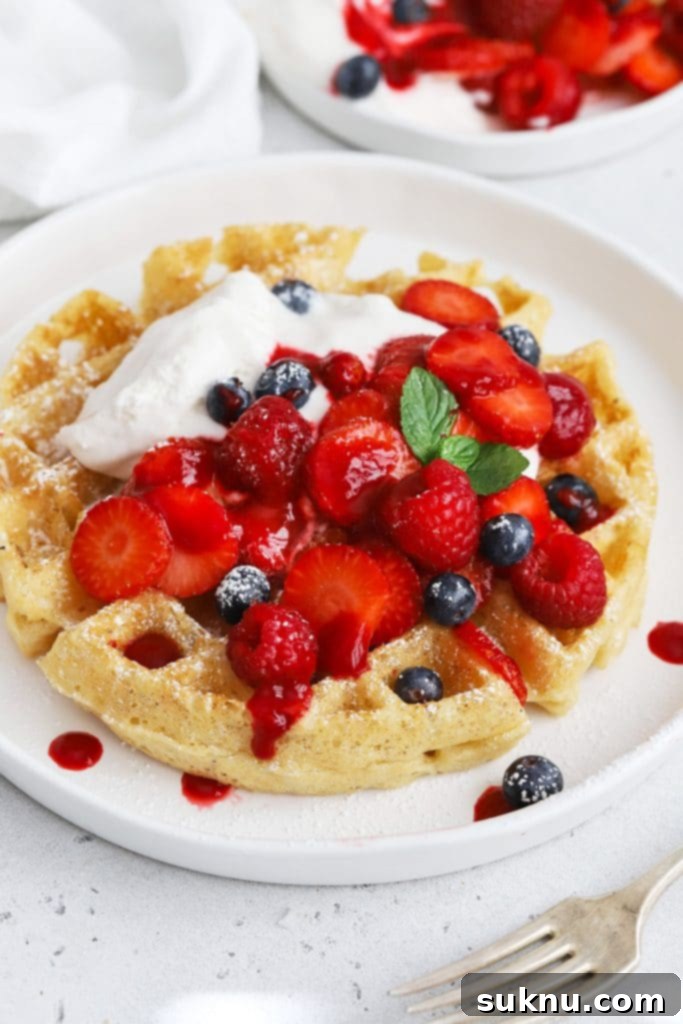 Front view of gluten-free Belgian waffles topped with berries, whipped cream, and raspberry syrup