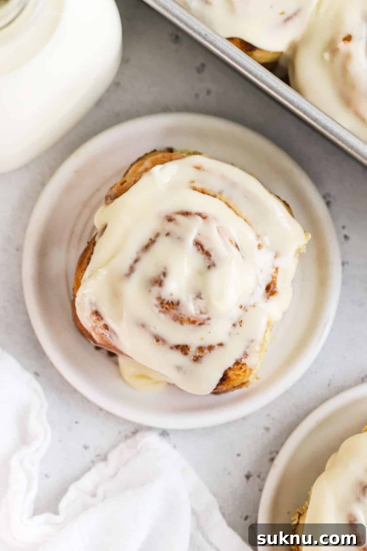 Gluten-free cinnamon roll on a white plate next to a bottle of milk, showcasing the soft texture