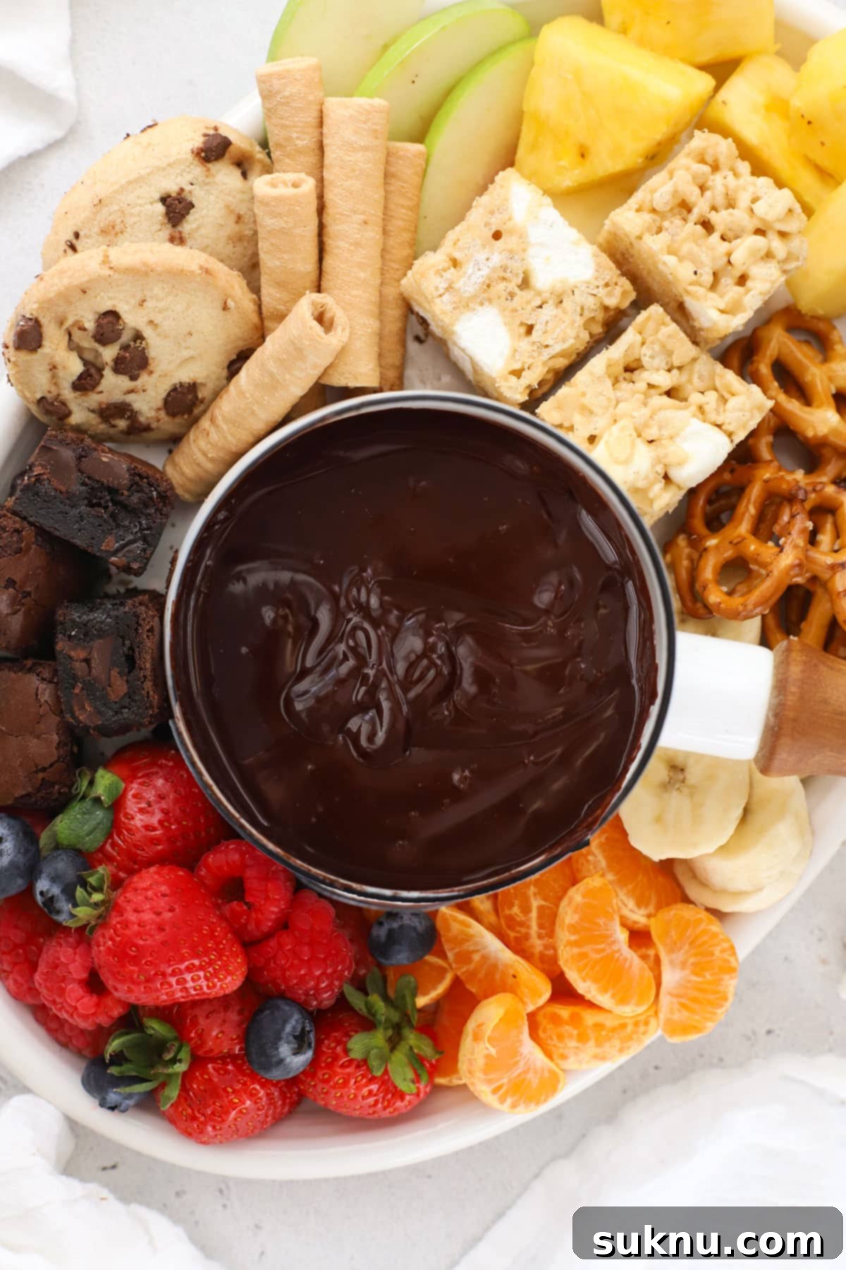 Gluten-free chocolate fondue surrounded by fresh fruit and an array of gluten-free dippers on a festive table.