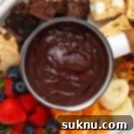 A small white pot of gluten-free chocolate fondue with fresh fruit and small gluten-free dippers around it.