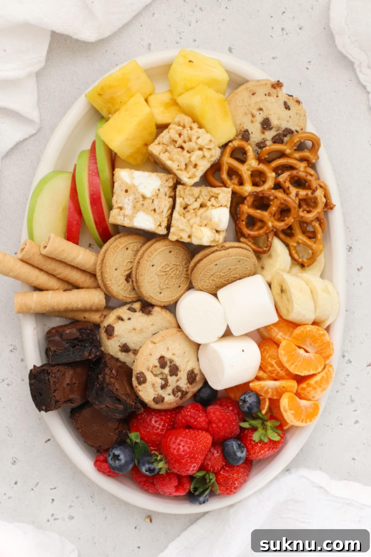 A vibrant platter overflowing with a diverse selection of gluten-free fondue dippers, including fresh fruit, cookies, and crunchy snacks.