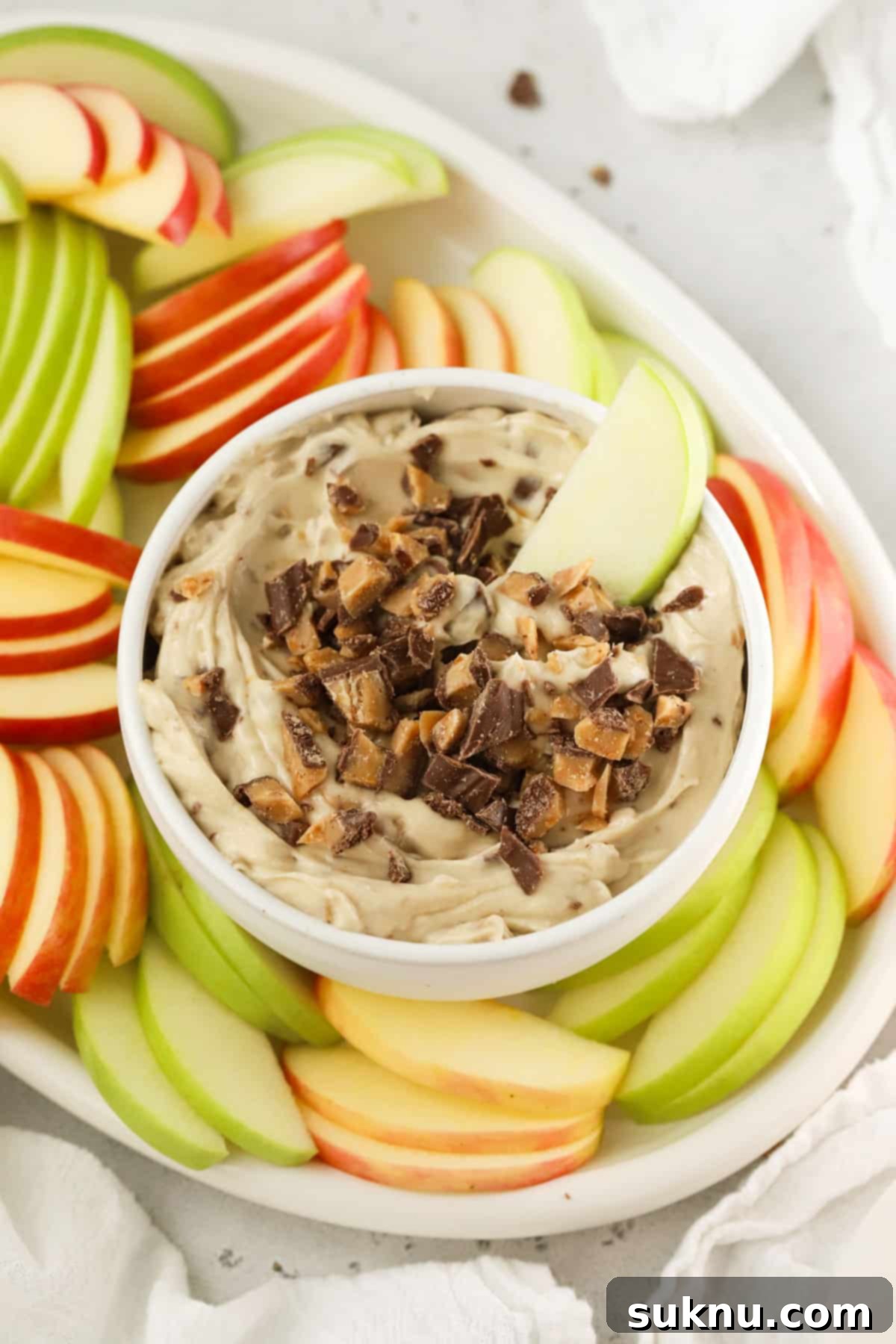 Dipping an apple slice into creamy toffee apple dip, highlighting its smooth texture and visible toffee bits.