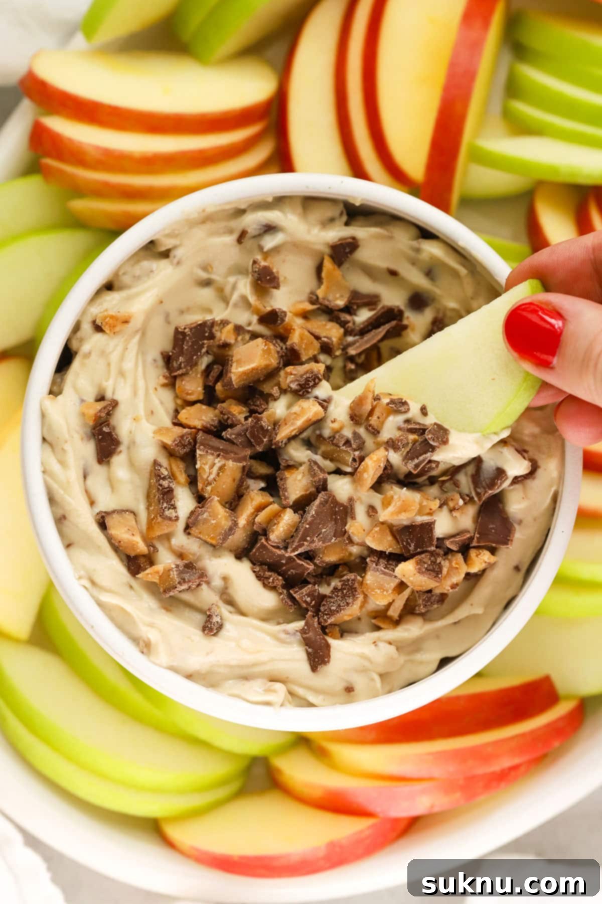 A person dipping a fresh apple slice into a bowl of creamy toffee fruit dip, showcasing the perfect consistency.
