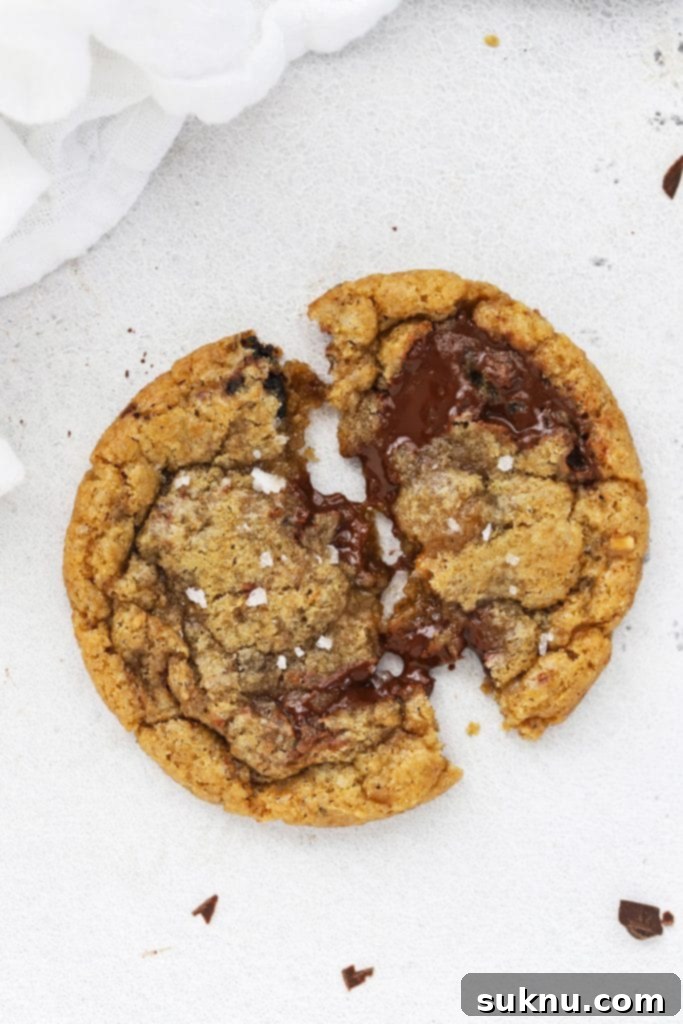 A gooey gluten-free brown butter toffee chocolate chip cookie being pulled apart, revealing its warm, soft center.