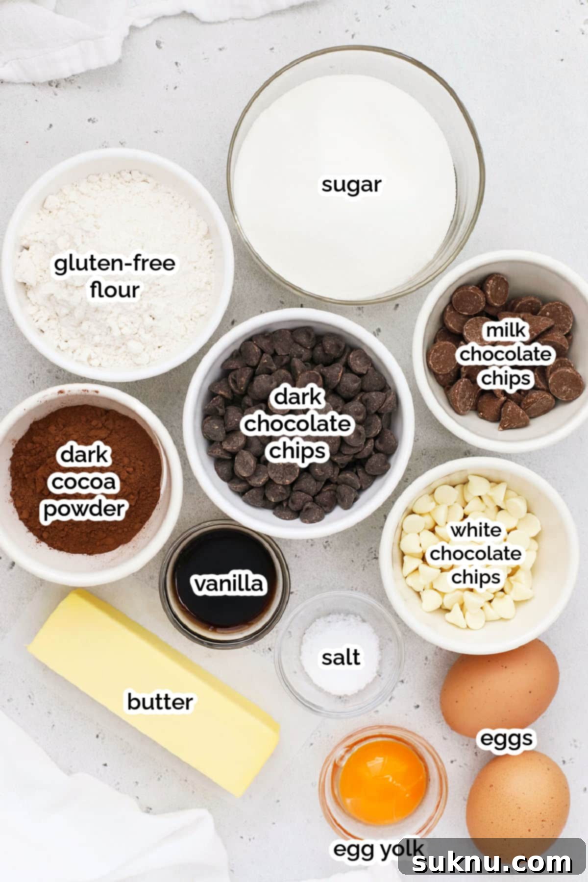 Arrangement of essential ingredients for making gluten-free triple chocolate brownies, including chocolate chips, butter, sugar, eggs, and flour.