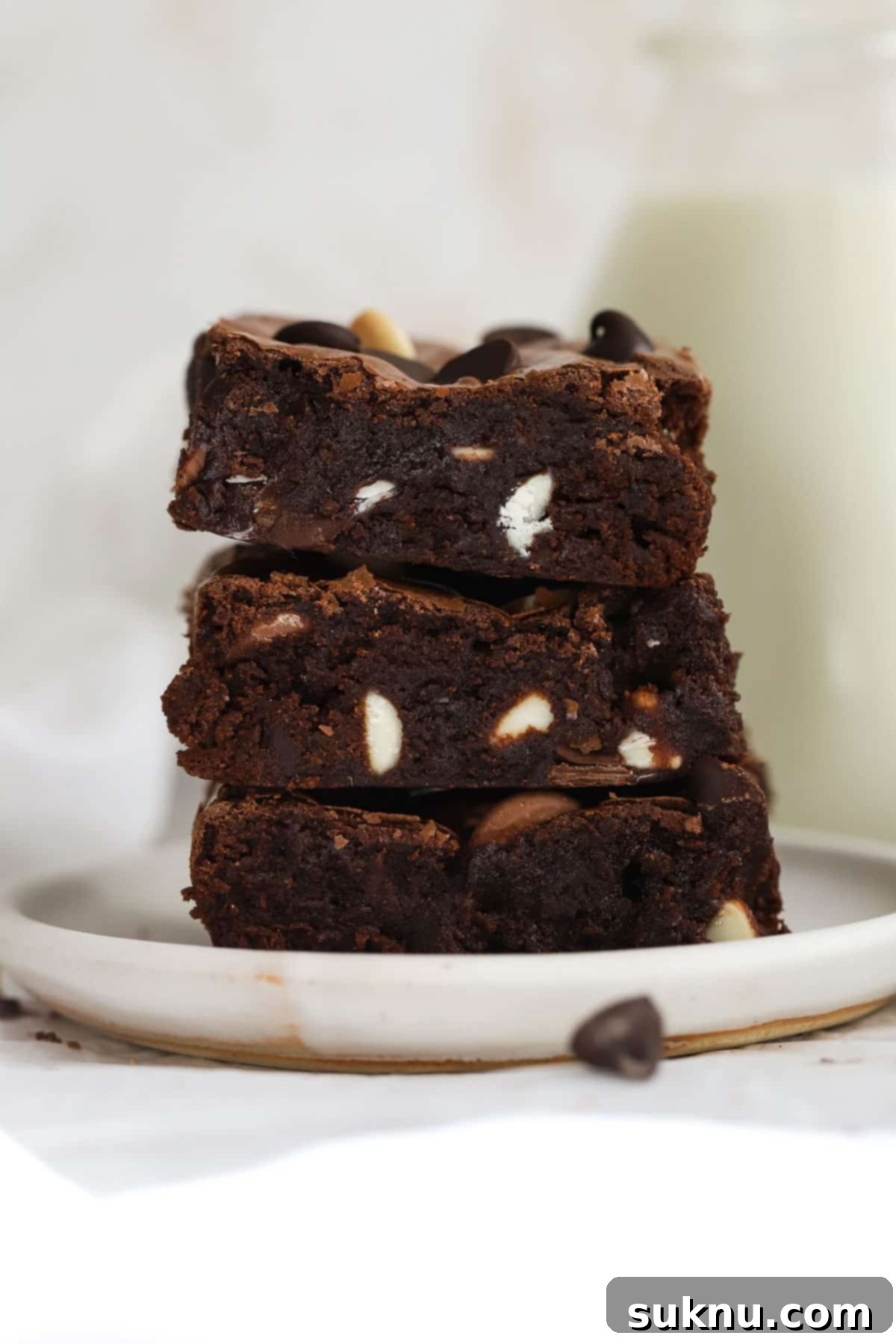 Stack of gluten-free triple chocolate brownies on a white plate, showcasing their fudgy texture and shiny top.