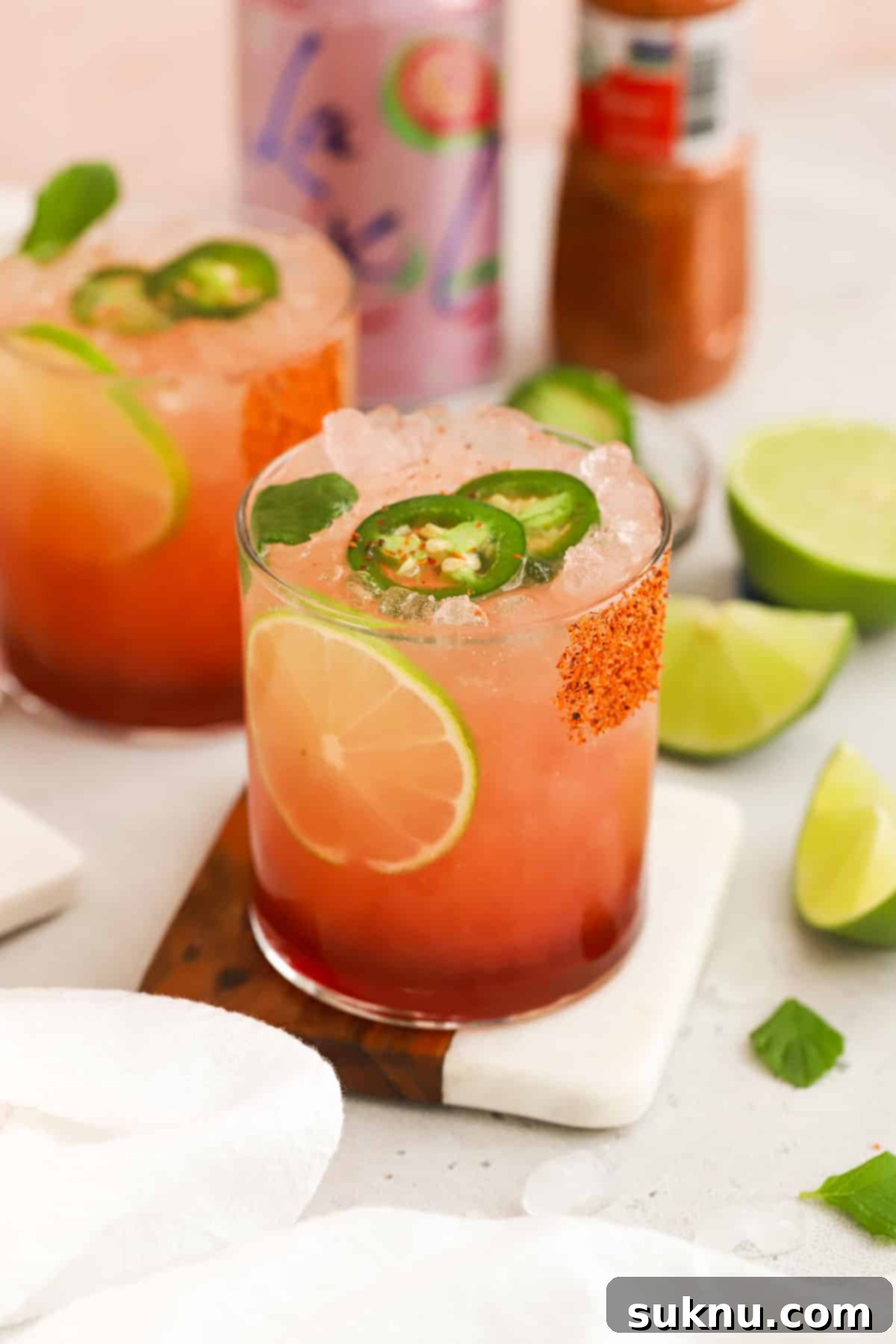 Two guava mocktails with lime and jalapeño garnishes, served on a rustic wooden board