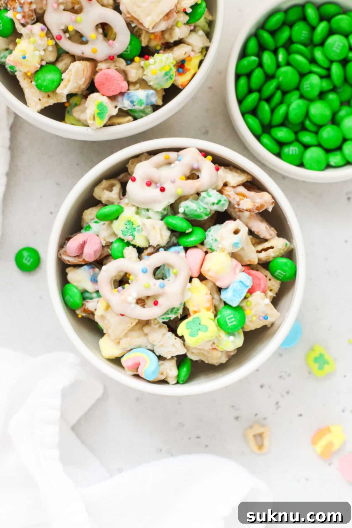 Two bowls of vibrant green and rainbow colored gluten-free leprechaun bait snack mix, with a smaller bowl of green M&M's nearby, set against a festive background.