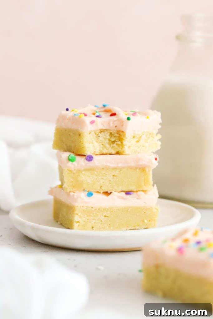 Decadent Gluten-Free Cadbury Blondies 8 Three perfectly frosted gluten-free sugar cookie bars, adorned with festive pink frosting, stacked on a white plate, showcasing their delightful appearance.