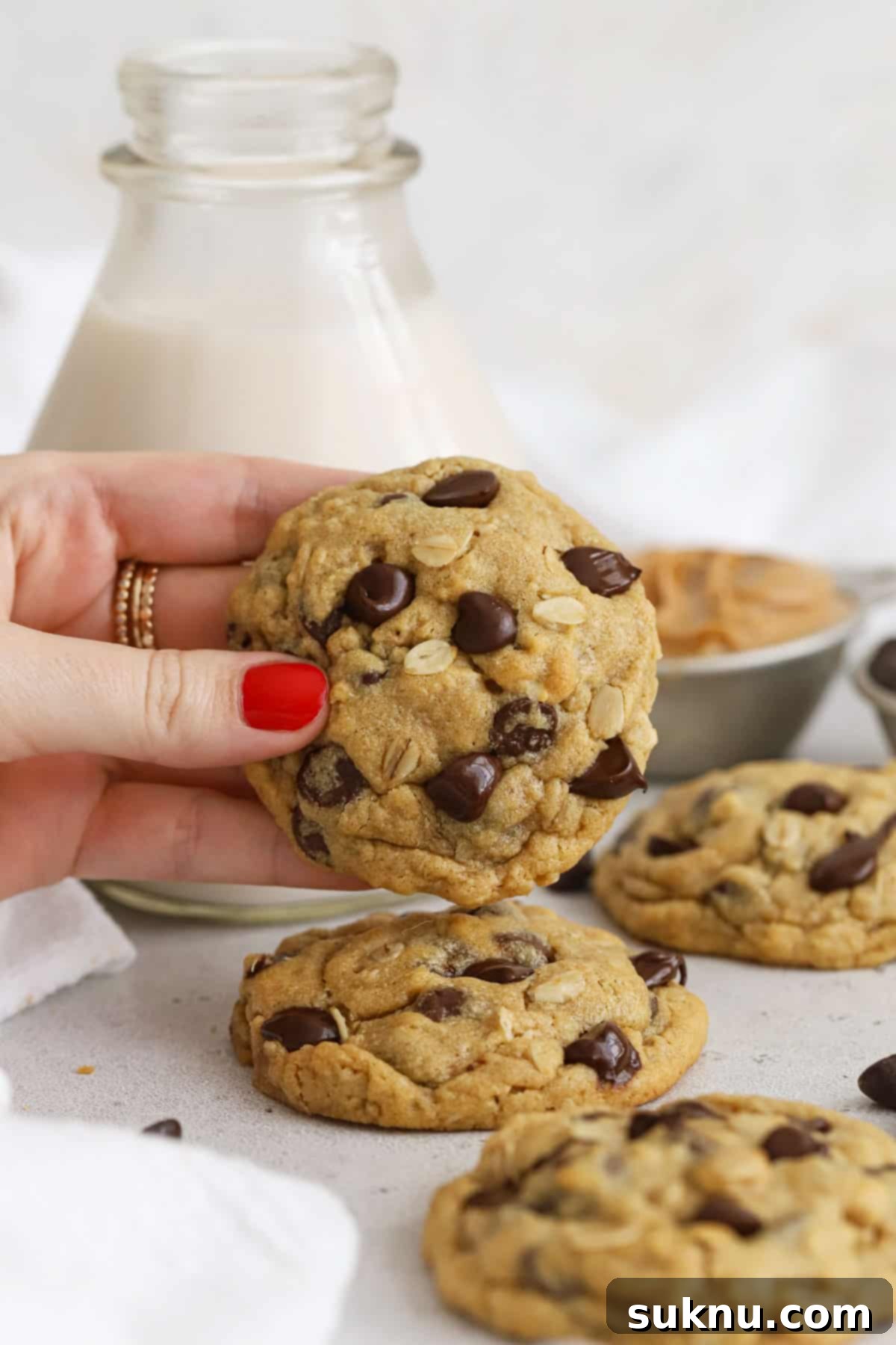 Gluten-Free Peanut Butter Oatmeal Chocolate Chip Delights 6 A hand holding a perfectly baked gluten-free peanut butter oatmeal chocolate chip cookie in front of a bottle of milk, highlighting its enticing texture.