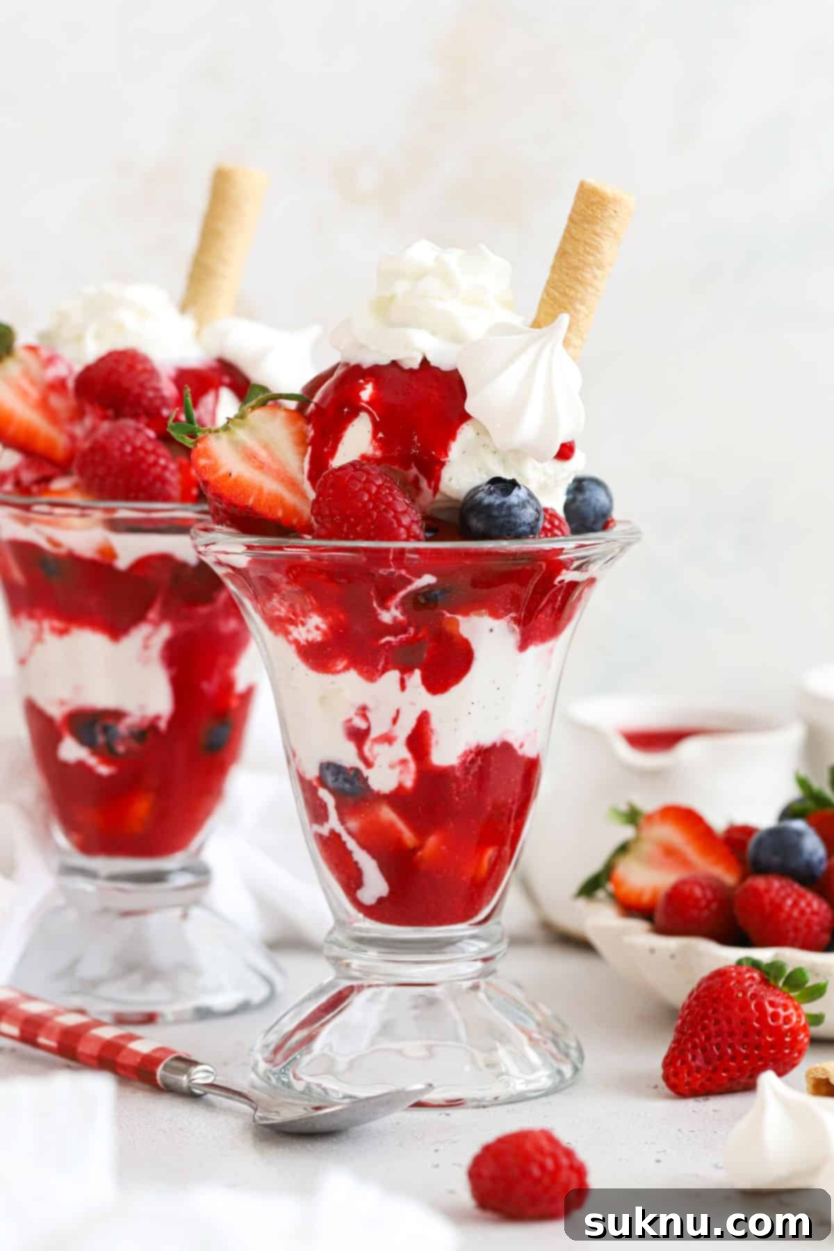 Homemade Knickerbocker Glory with vibrant raspberry sauce, fresh berries, whipped cream, and meringue
