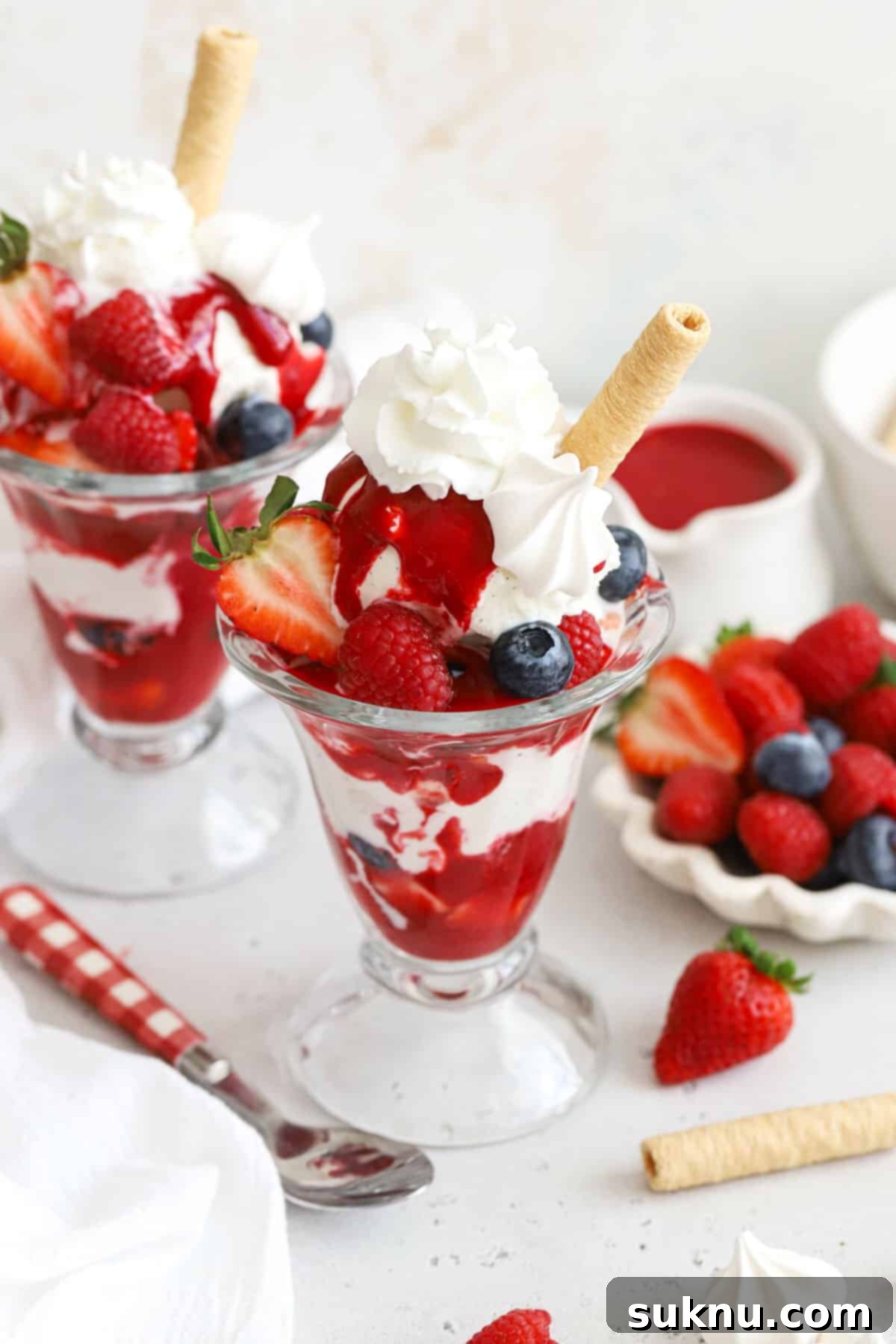 Homemade Knickerbocker Glory sundae in a tall glass, with raspberry sauce, fresh berries, whipped cream, meringue, and a coconut roll