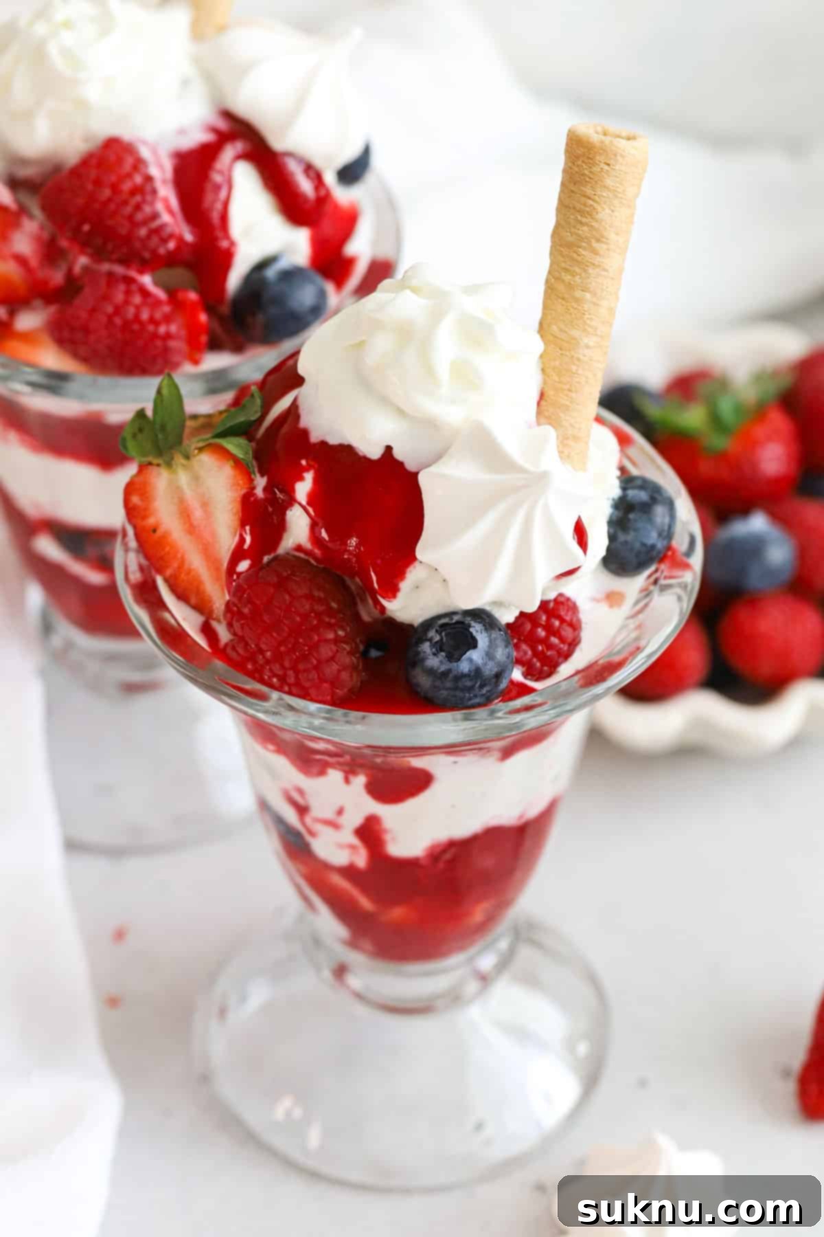 Mixed berry Knickerbocker Glory topped with whipped cream, meringue, and a coconut roll, ready to be enjoyed