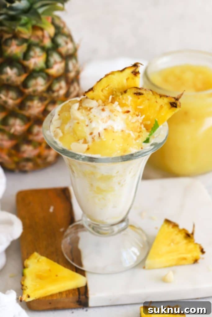 Tropical ice cream sundae with pineapple topping, fresh pineapple, toasted coconut, and macadamia nuts