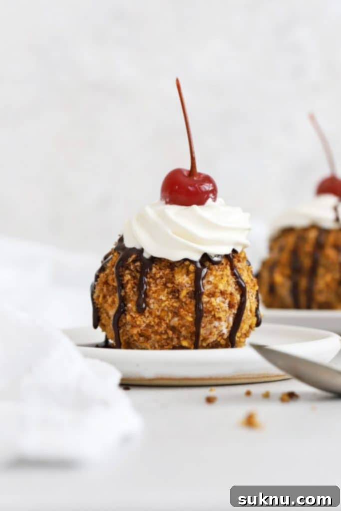 Front view of gluten-free fried ice cream topped with whipped cream, chocolate syrup, and a maraschino cherry