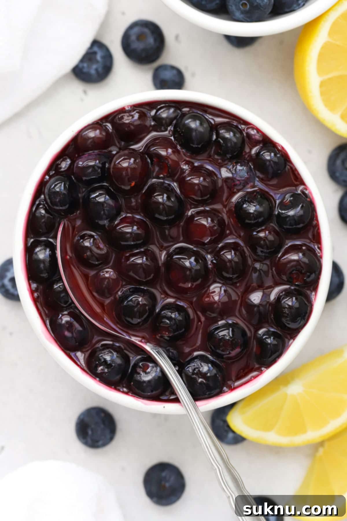 Easy Blueberry Sauce For Cheesecake And Beyond 2 A spoon delicately dipping into a bowl of fresh, vibrant blueberry sauce, showcasing its rich texture and inviting color.